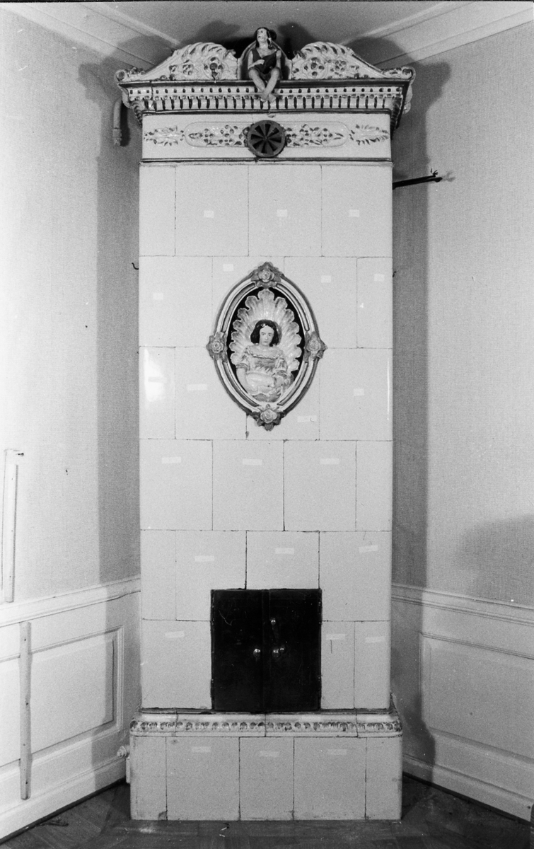 Kakelugn i vitt, med inslag av guld och polykrom dekor. Hög och fyrsidig. Bestående av sammanfogade, rektangulära plattor. Framsidan med oval nisch, i form av polykrom och förgylld medaljong, med dekor av "sittande flicka med hund i famnen framför musselskal". Ramen delvis förgylld samt med fyra rosor. Kakelugnens krön, med lutspelande sittande figur, flankerad av böljande blad- och volutformade ändar. Nedanför krönet, rosett- och bladornamentik inom förgyllda lister, samt ventilationslucka av mässingsplåt. Längst ned luckor i järnplåt. Delarna förvaras i trälådor.

Äldre historik: 
Kakelugnen härstammar troligen från en gammal byggnad, som förstördes i sista branden 1877 i Borås.

Funktion: För uppvärmning av bostadshus