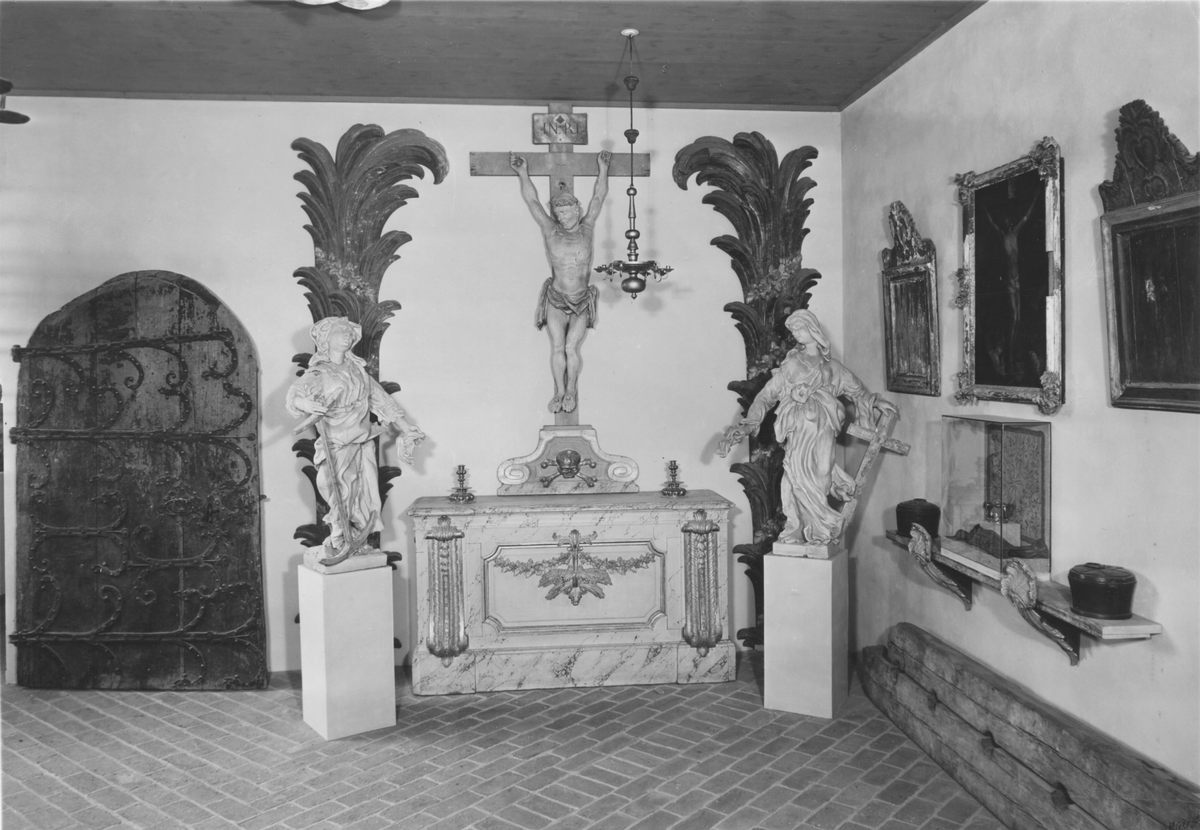 Kyrkdörr, romansk, kyrkport, med järnornament och beslag. Dörren består av tre lodräta, tjocka furuplankor, rundad upptill. Tre kraftiga gångjärn. I övrigt rikligt järnbeslagen. I ändarna av beslagen på en del ställen gapande djurhuvuden. Spår av tjära. Flera ristningar, bland annat armborst, konsekrationskors (invigningskors).