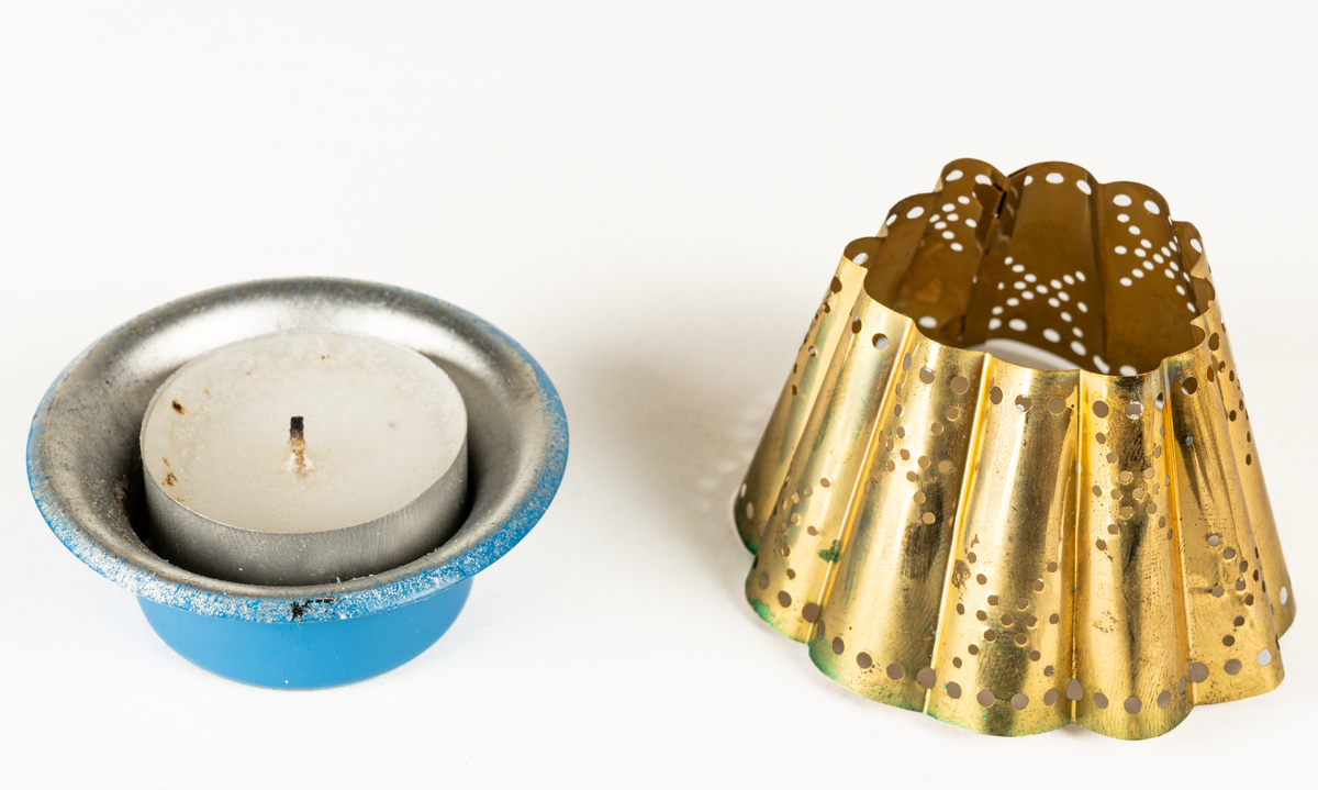 Ljuslykta för levande ljus, s.k. kuvertlykta. Blå fot med plats för ljus, vågig skärm, perforerad. Tillhörande röd ask i papp.