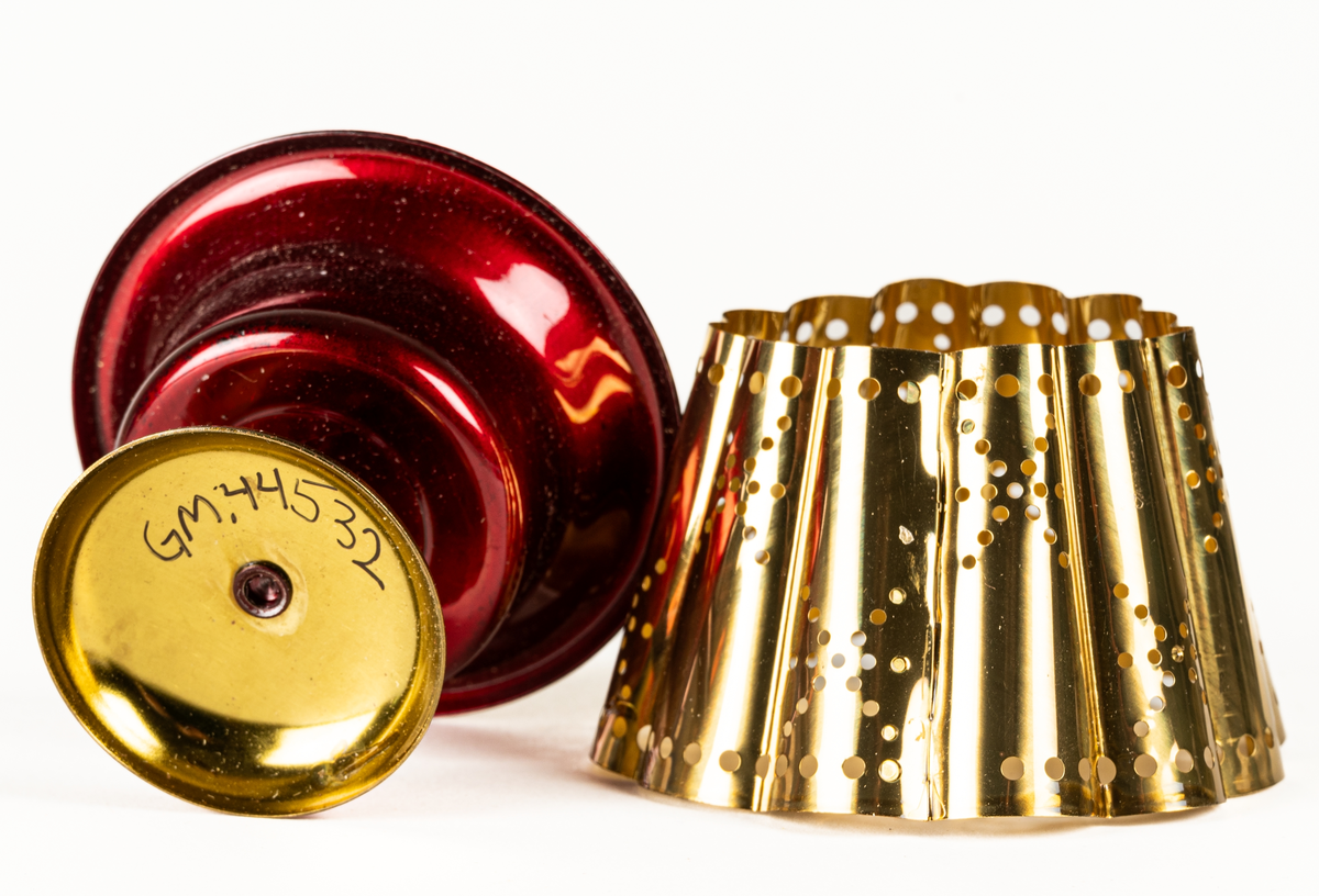 Ljuslykta för levande ljus, s.k. kuvertlykta. Röd fot med plats för ljus, vågig skärm, perforerad. Tillhörande blå originalask i papp.