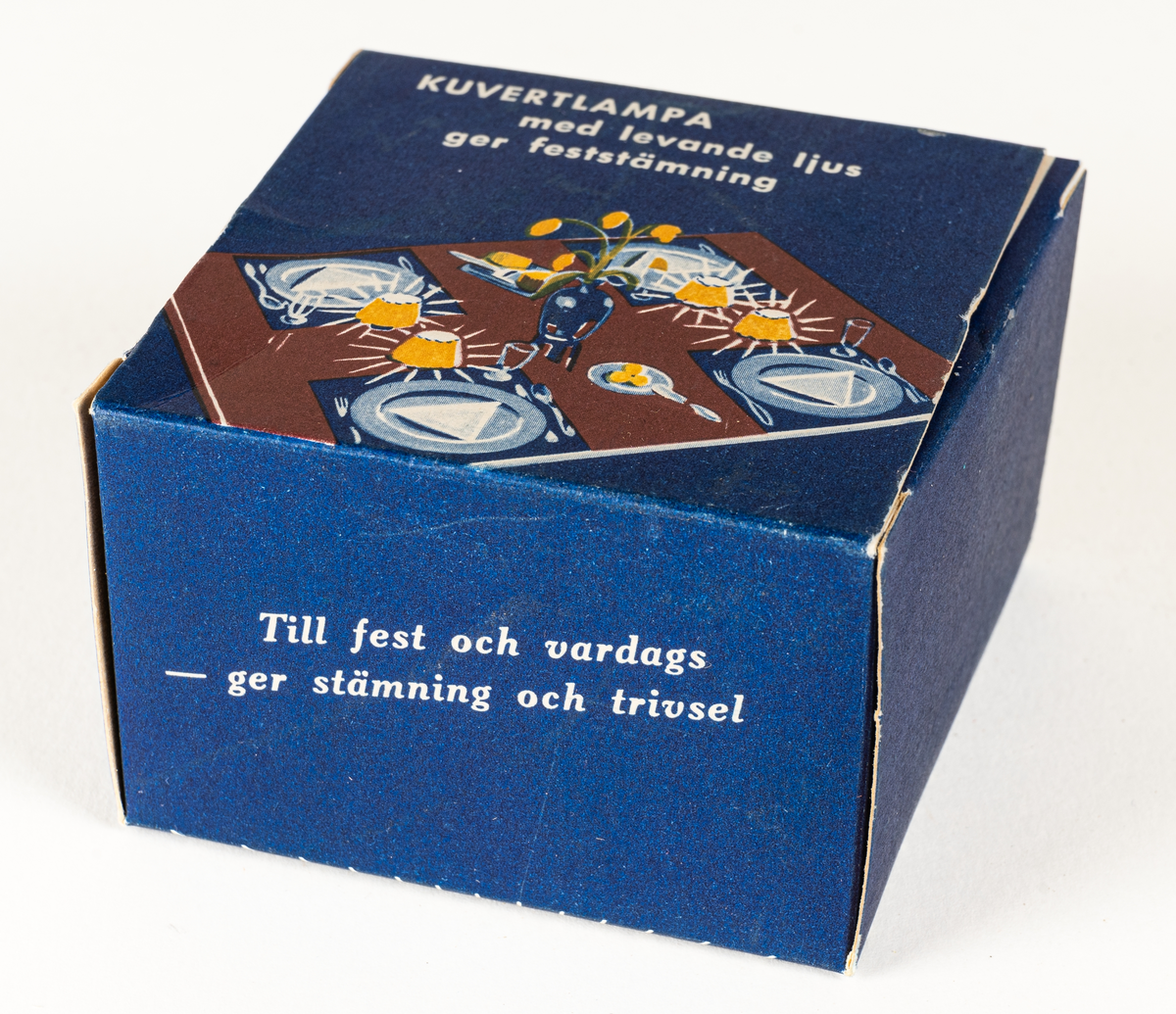 Ljuslykta för levande ljus, s.k. kuvertlykta. Röd fot med plats för ljus, vågig skärm, perforerad. Tillhörande blå ask i papp.