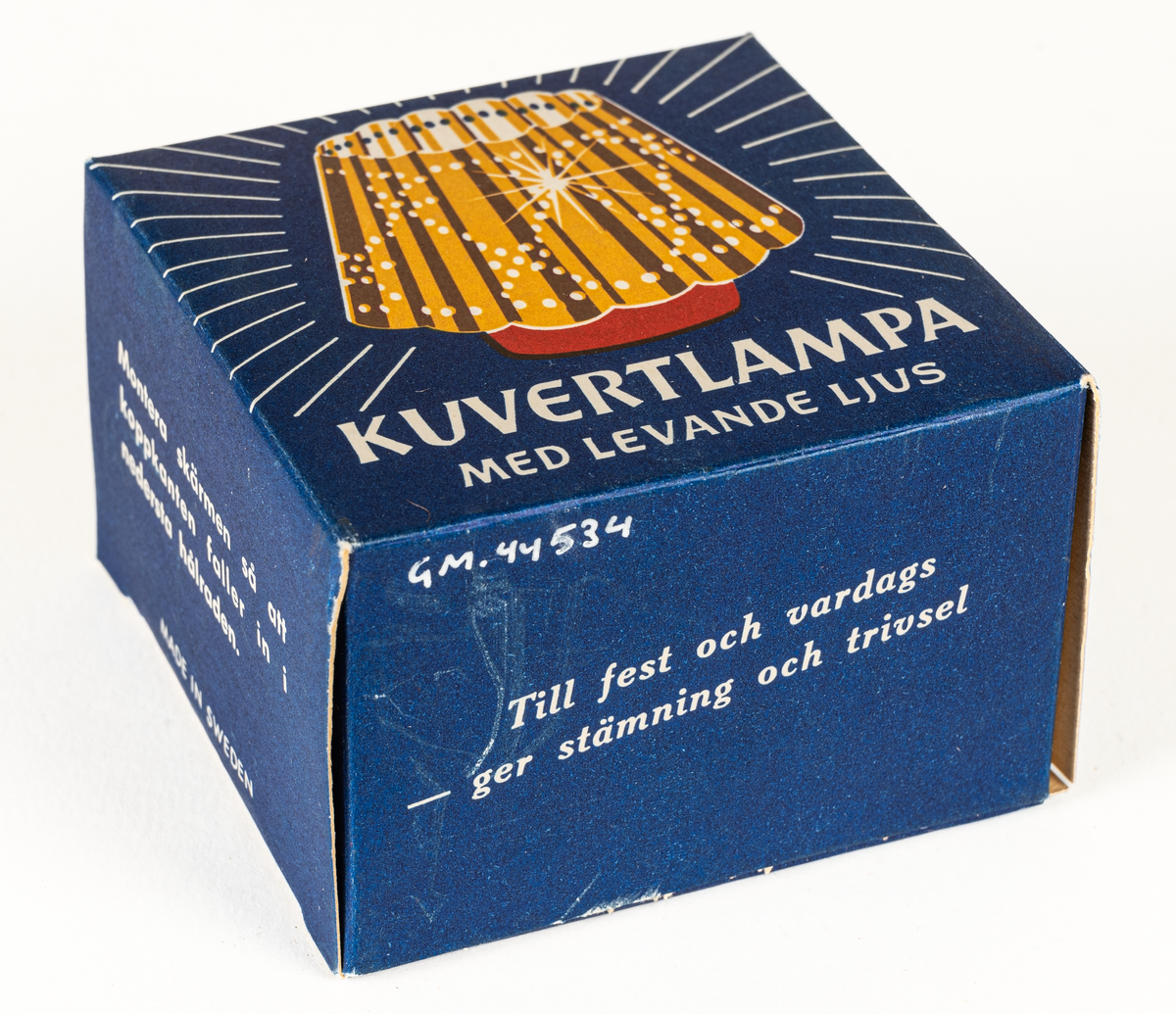 Ljuslykta för levande ljus, s.k. kuvertlykta. Röd fot med plats för ljus, vågig skärm, perforerad. Tillhörande blå ask i papp.