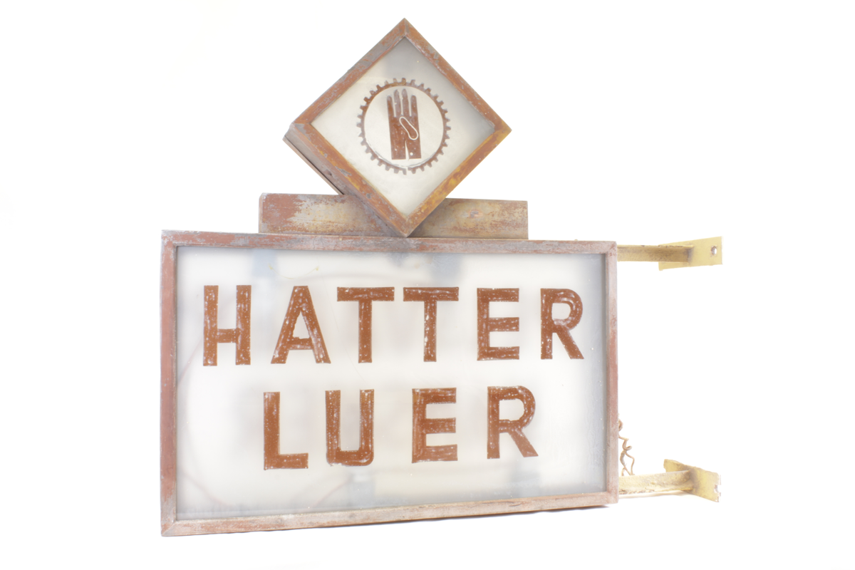 Utendørs skilt for salgslokalene til R. Tronsmo & Sønn i Glommengata i Kongsvinger. Skiltet består av frostet glass med logo og tekst, og har innvendig lysarmatur med fem lyspærer.