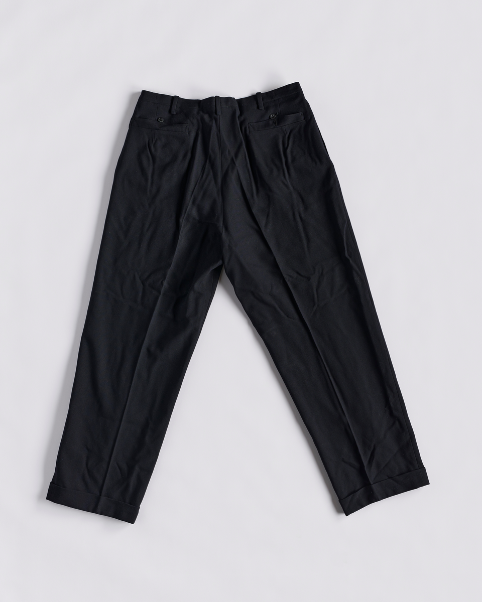 Dressbukse i bomull. Gylfen lukkes med 6 knapper og en hekter. To baklommer og to stikklommer foran. Ved linningen er det en liten lomme med klaff. Smygstoler i linningen til belte. Knapper på innsiden av linningen til bukseseler. Brett nederst på buksebeina.
