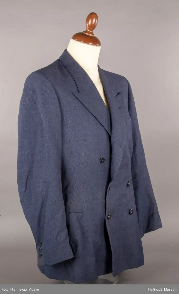 Blågrå dressjakke med slag og dobbel rad med knapper, 3 knapper på hver side. En brystlomme på venstre side, 2 jakkelommer uten klaff. 3 knapper framme på hvert erme. Foret med svart tøy av kunstsilke. En liten innerlomme. Jakka har antagelig tilhørt skredder Odd Navrud.