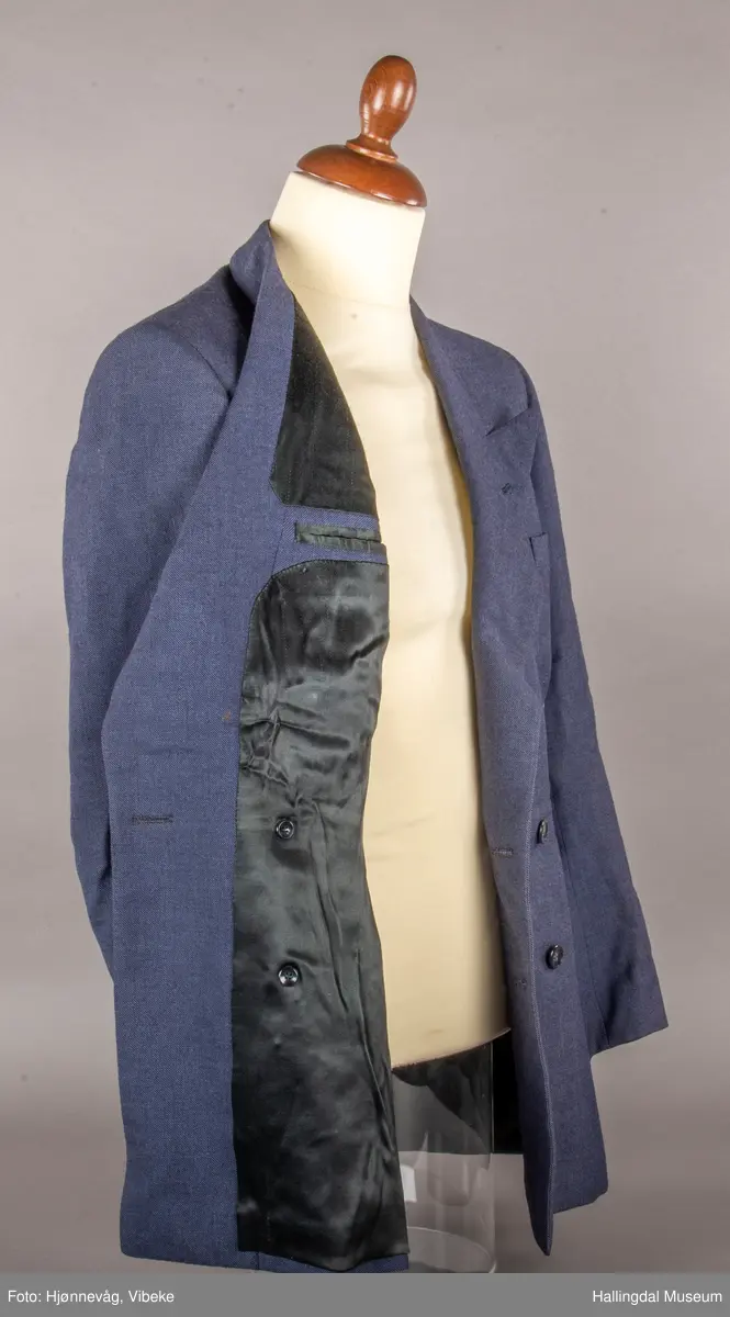 Blågrå dressjakke med slag og dobbel rad med knapper, 3 knapper på hver side. En brystlomme på venstre side, 2 jakkelommer uten klaff. 3 knapper framme på hvert erme. Foret med svart tøy av kunstsilke. En liten innerlomme. Jakka har antagelig tilhørt skredder Odd Navrud.