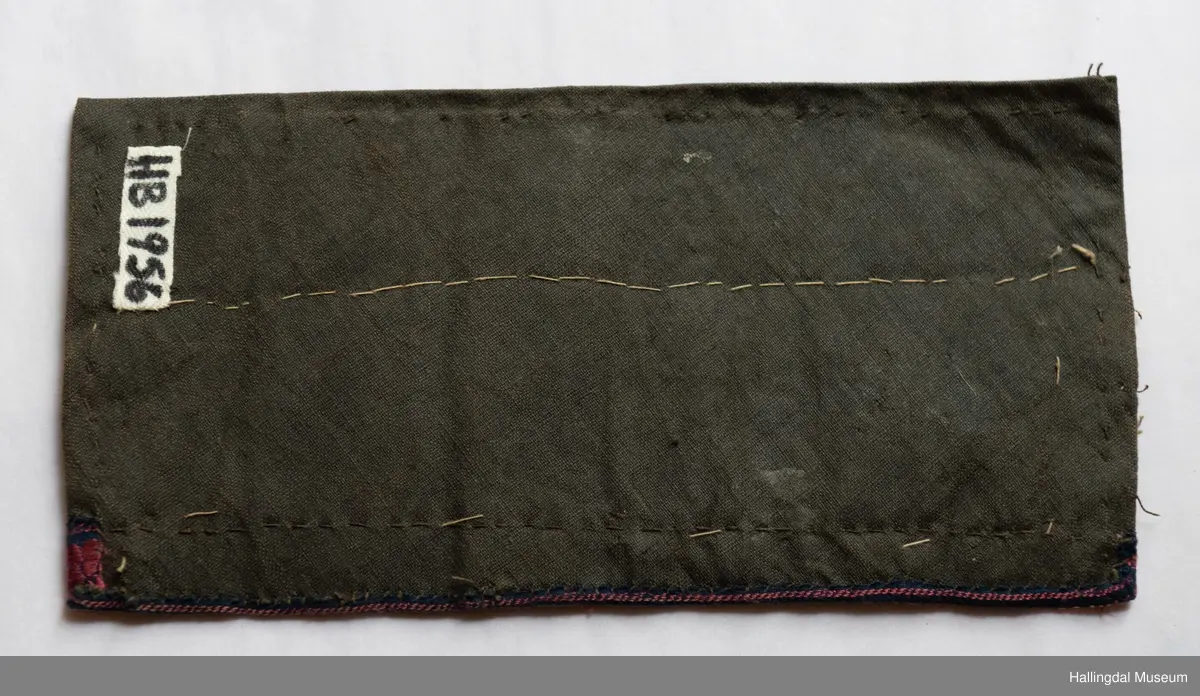 Voksduk med mønster i gull og grått. Påsatt bred sølvknipling. Øverst blomsterete bånd. Foret med sort tøy. Tråklesting i sort og hvitt.