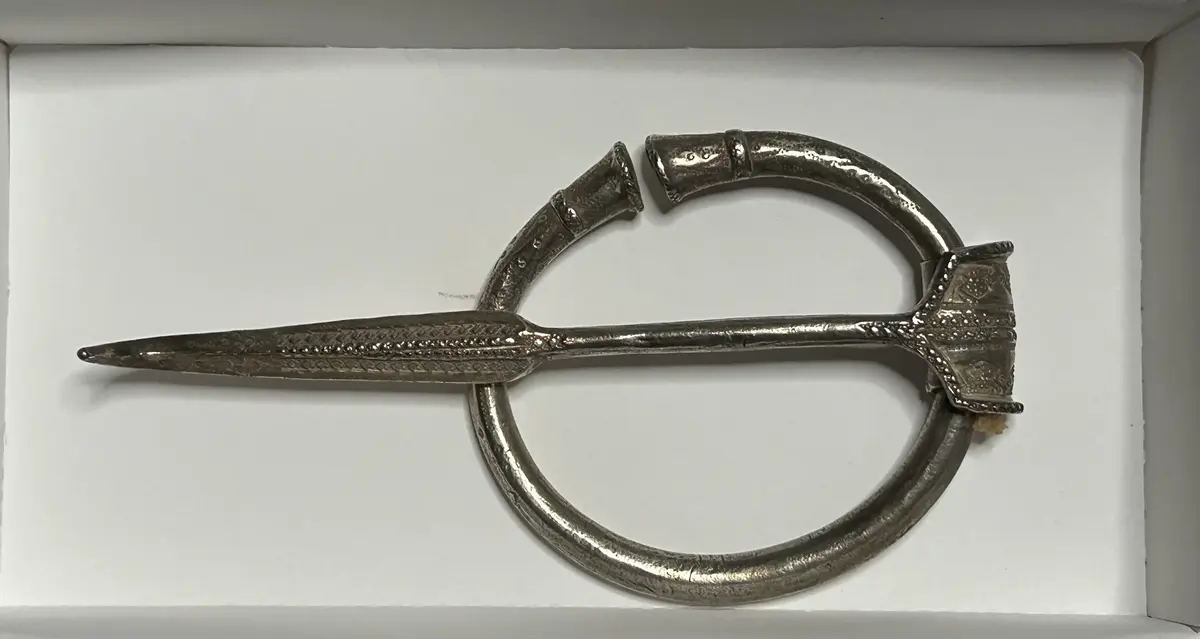 AV SILVER, AV RUND TEN, TRUMPETFORMIGT AVSLUTADE ÄNDAR, LÅNG NÅL MED STÄMPELORNERAD UPPRULLAD DEL. NÅLSPETS, UPPBÖJD MED RIK STÄMPELORNERING. STORLEK 9 x 8 CM. NÅLENS L. 16 CM. FRÅN KARLS I TINGSTÄDE. PÅTRÄFFAD VID HARVNING, VÅREN 1972, CIRKA 50 M. SÖDER OM FYNDPLATSEN, FÖR KARLSSKATTEN ( C 10396), SE ÄVEN C 10 774: 1-2 OCH C 10 832. VER. NR: 496.