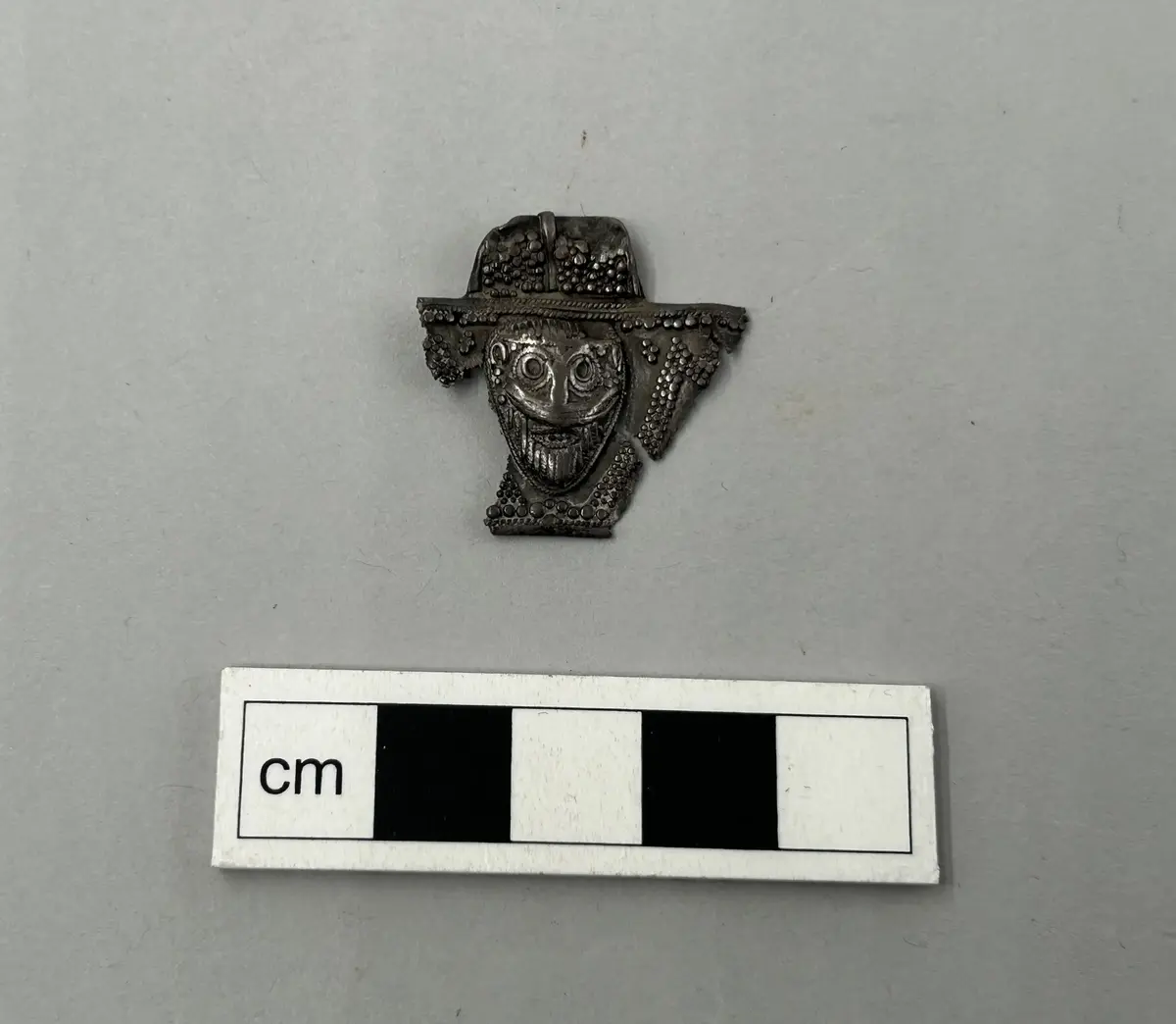 DEKORERAD, MED ANSIKTSMASK. RIKT DEKORERAD MED PÄRLOR AV SILVER. STARKT SKADAD. BRUTET. H. 26, BR. 2,6 CM. FRÅN RUTE SN. KAUPARVE, TILLHÖR TIDIGARE SKATT.