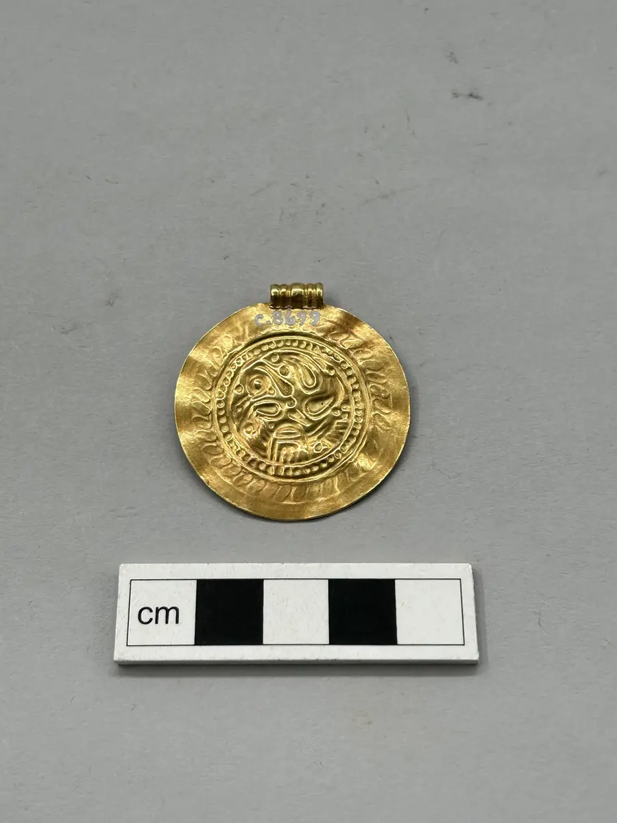 Gotländsk e-brakteat av guld med stämpeldekor och triskelmotiv i centrum.enbart Präglad på ena sidan kompl mars 2006/ml
av guld med ögla. Funnet vid jordbruksarbete vid s:t västergårda i fide, av lantbr. Helge jakobsson, s:t västergårda. Inköpt för  60 kronor och skänkt till gotl. Fornsal av fru ada block, visby.  Med riksantikvariens medgivande tillförd gotl. Fornsals samlingar, konc.nr. 71/36, 80/36, 97/36, 110/36, dnr. 82/36