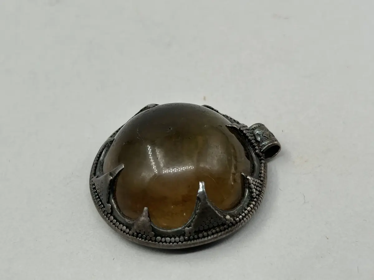 Hänge av bergkristall, halvsfärisk, gulaktig  kristall infattad i silver med upphägningsögla. Baksida i silver. 
Lämnades till museet tillsammans med "Fröjelkulan" GFC20139_1  
nyreg nov 2006/ml