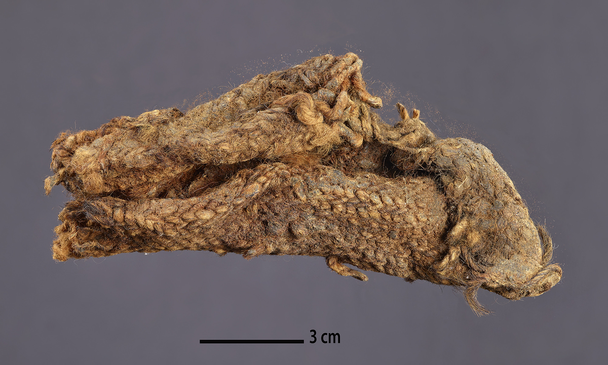 2 tekstil fragmenter, Sammenkrøllet tekstil fragment + tresidig tekstilflak. (tidligere merking T05A og T05B), samt to prøver (tidligere merket T05a og T05b).

Funnet på samme sted som Ts16187.1. Jon Godal beskriver det som om det kan stamme fra et hjørne, og spør om det kan være rester av likninggarn som er satt inn i duken. Inne i bretten av tekstilet ser han søm hvor to kanter er sydd sammen. Folden inneholder også rester av "seilsmøring". To fragmenter av Ts16187.5 underkastes analyse. Fragment (a) er brettet, 15 cm langt, og måler 7 cm på tvers (foldet). Rester av hyssing (likningsgarn) stikker ut, og fragmentene er klissete med tjære eller annen smøring. (b) ble avskåret (a) i 1991, og har blitt gjenstand for konservering og analyse av Susan Möller-Wiering.
Analyse (svensk tekst): Varp: ca. 6-7 tr/cm (ca. 13 på 2 cm), Z-spunnet tråd, hardt spunnet, 1-1,2 mm i diam. Innslag: ca. 4 tr/cm, S-spunnet,  ser ingen - løst - middels spunnet, 2-2,5 mm i diam. Varpeffekt 2/1 høyrekypert (høyrediagonal). Pigemterte hår, mer i varpen enn i innslaget. Varpen jevnt spunnet, innslaget er ujevnt. 

Analyse (dansk skrift) Fragment a er sammenkrøllet, 15 cm langt og ca. 7 cm bredt, innkrøllet tilstand, innfettet i tjære. b er tatt ut av fragm. a og konservert av S. M-W. 19 x 14 cm, bevart ?? i kortside. Uregelmessig skjært av. Børstet/valket på kortside