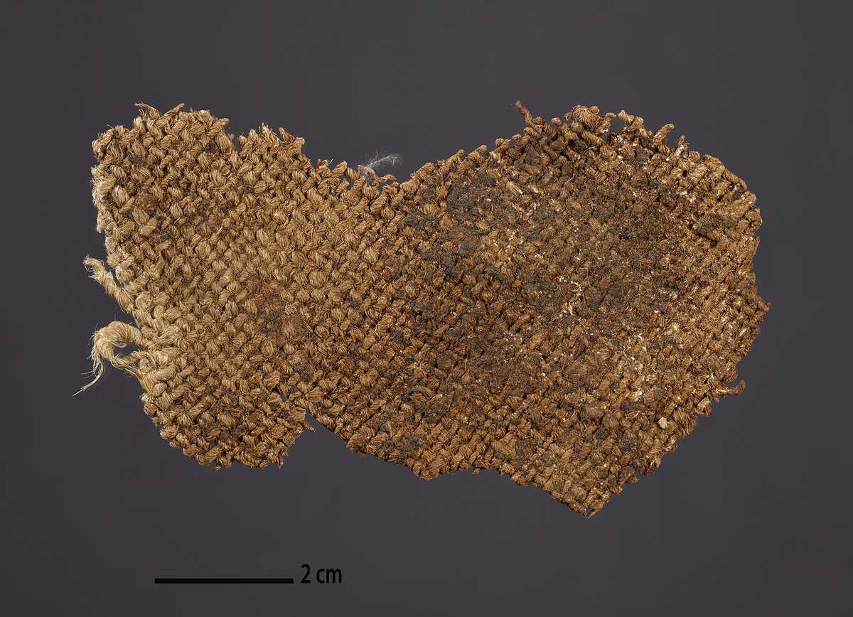 Tekstilfragment (tidligere merket T15).
I enkelte skar høyt oppe i taket var det duk av en annen kvalitet enn det som dominerte. Det lå enkelte fragmenter av disse på golvet over koret. Det er tolket å være lerretsvev og fremstilt av plantefiber. Det kan se ut som om både renning og veft er høyrespunnet.