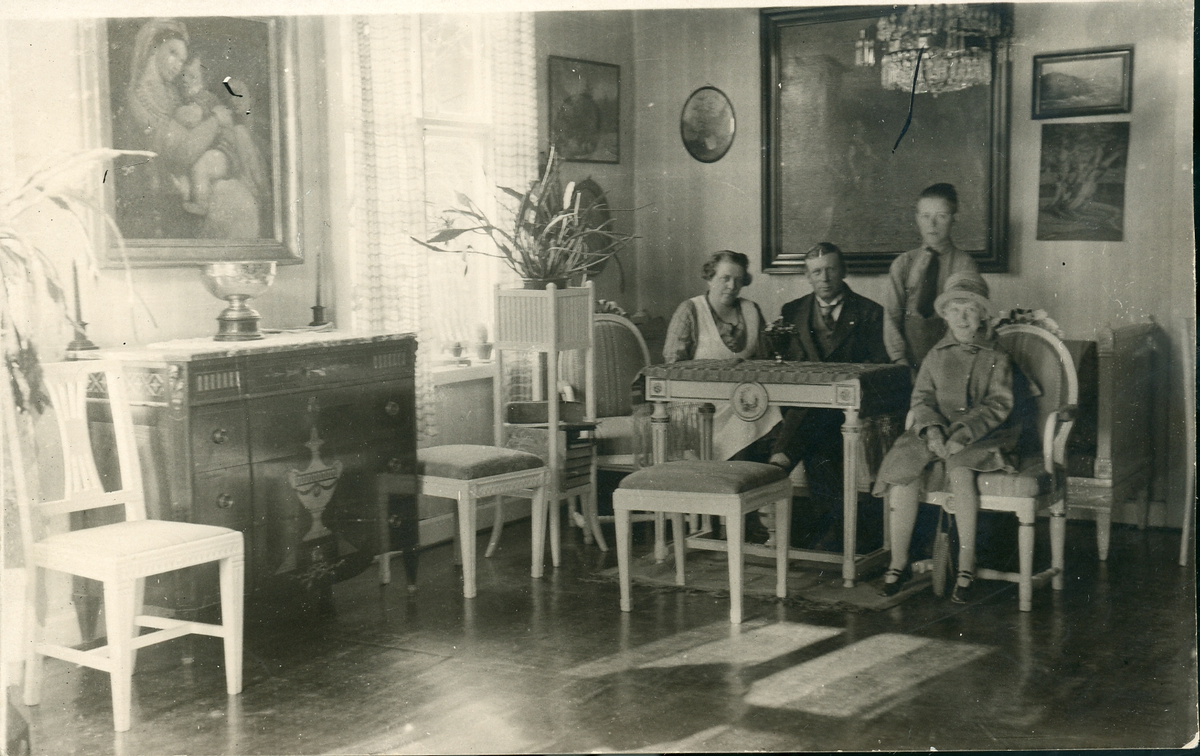 Svartvit fotografi av fyra person, två vuxna, man och kvinna, samt två barn, [möjligen avsändarens] i finrum.