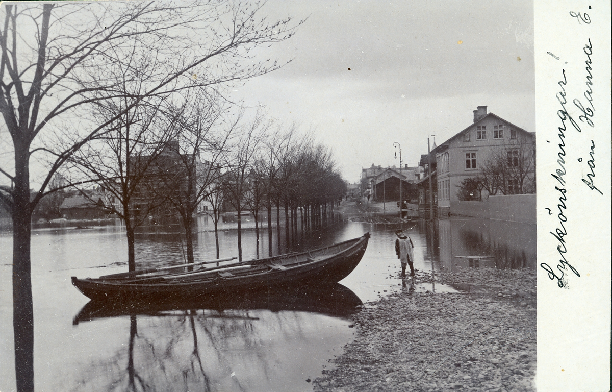 Svartvit bild föreställande ett översvämmat stadslandskap med en eka och ett barn i bildens förgrund.