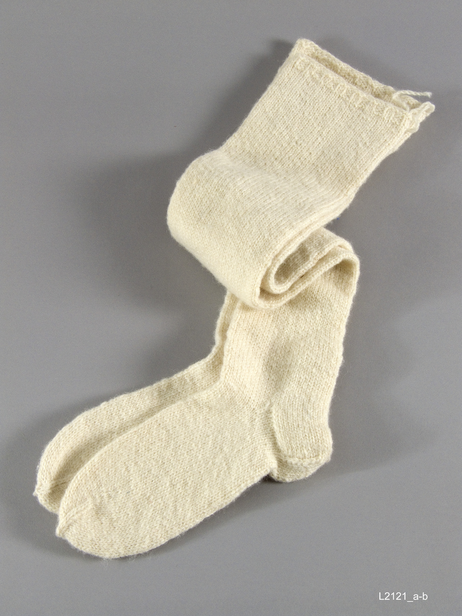 Ullester Hvite lange ullester, 1 cm vrangbord, "figurstrikkete" - smalast ved ankeln. Skaftets lengde 62 cm Fotens lengde 26 cm Tradisjonellt sjøsamiskt strikkearbeid strikket av Mary Myrhaug f. 23.6.25 Biertav&#x00E1;rri, Kåfjord Troms . Innkjøpt av J.A.K. 1987.