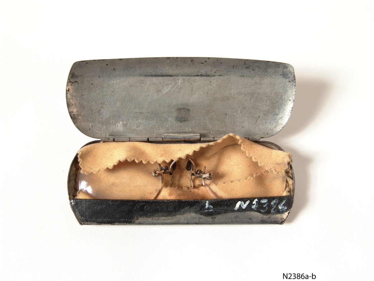 1 Lorgnett a), med futteral b), a) Lorgnetten av gull (?), 2 sirkelformete glass . Hel lengde 10,2 cm. futteral, metall, lokk festet med hengsler, stykke sort tøy  ved lokket, lyst pusseskinn nedi, merket "Optiker Sigurd Tvedt, Kristiansand S. telf: 3427" og tegning av et par briller. l : 11,4 cm br : 4,5 cm h : 1,0 cm. (utvendig målt)