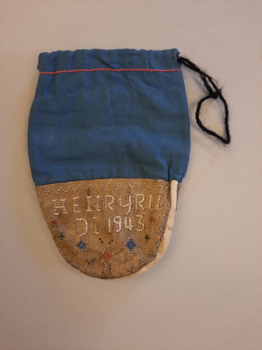 Tekstil og skinn pung. Foran står det på første linjen: HENRYRU, på andre linje: DI 1943. Den er dekorert foran og bak i rødt, blått og lyst beige. Tekstilet er blått. Nært kanten øverst er det brodert en rød kant med tråd. 
Henry Rudi var svært flink i all salgs hådverk. Under overvintringene lagde han mange ulike håndverksprodukter. 