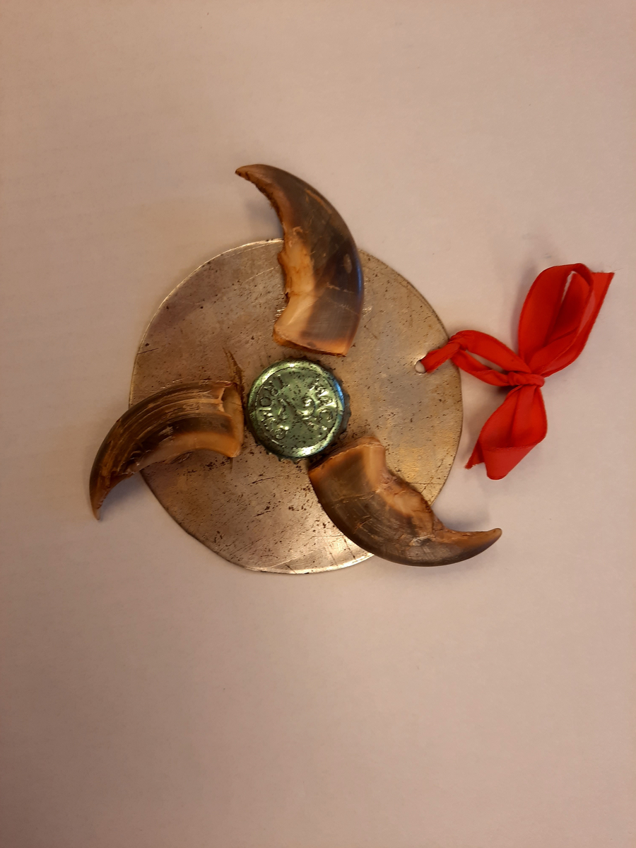 Æresmedalje som Henri Rudi mottok da han ble æresruss i 1969. Æresmedaljen består av en rund metallplate. På platen er det festet tre isbjørnklør med en Mack-kork i midten. På korken står det "Mack 2 Tromsø". Øverst på medaljen er det festet et rødt bånd. 