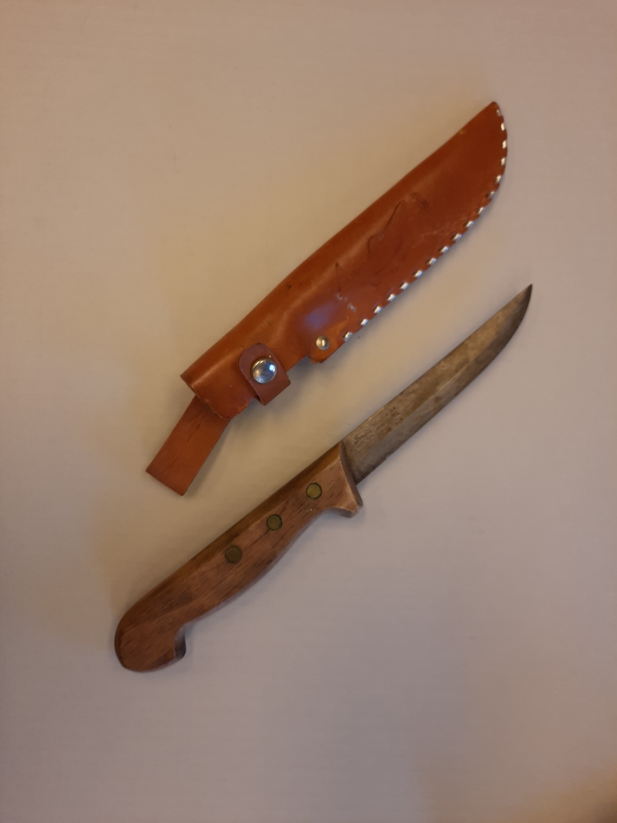Kniv tilhørt Halfdan Jakobsen. Kniv med treskaft, stålblad og lys brun lærslire. Sliren har en trykknapp for å feste den til kniven. 