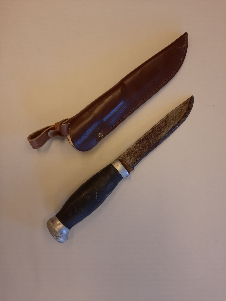 Kniv tilhørt Halfdan Jakobsen, med brun slire av lær. Svartmalt treskaft, med metall på hver side. 