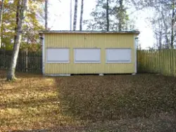 En ljusgul igenbommad ekonomibyggnad (kiosk med tre luckor) 