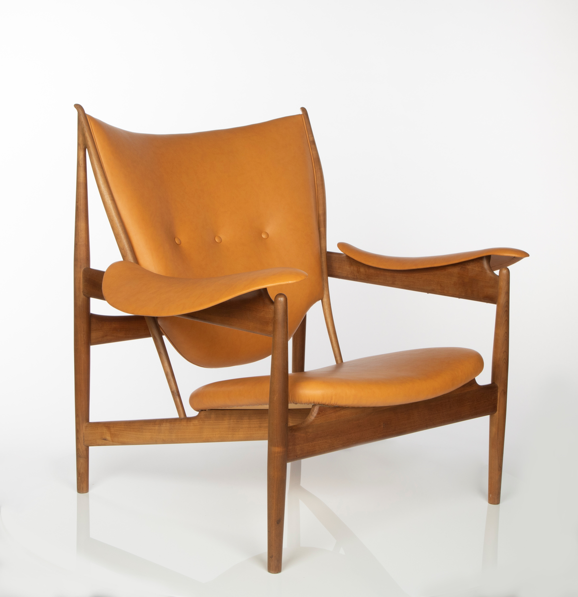 Stol, utført i brasiliansk valnøtt (imbuia). Åpen konstruksjon med fire runde ben, med størst tykkelse på midten, helt vertikalstilt. For- og bakben er forbundet med kraftig tverrligger som danner støtte for armlenene av buede stålplater. Mellom forbenene en bred sargsprosse som tiltar i høyde mot midtpartiet hvortil setets forkant er festet. Denne sprosse opptar i seg to kraftige, skråstilte og horisontale setestøtter fra bakbenene, og disse gir igjen feste for to spinkle, runde ryggstøtter som øverst møter bakbenene i en spiss vinkel, avsluttet med en liten knottforlengelse. Kraftige støttesprosser mellom bakbenene i rygghøyde samt kort tverrstøtte mot ryggplaten. Sete, rygg og armlener er fint og komfortabelt buet og trukket med lys oksehud. Stopning i sete og rygg. Både sete og armlener har få konsentrerte festepunkter til trekonstruksjonen og er skjult på undersiden. Dette gir sete og armlener en lett svevende virkning, som også understrekes av at setebredden er mindre enn trekonstruksjonens sitteåpning. Stolen har treets naturlige brune farge, med glattpusset overflate og avrundede kanter og hjørner.