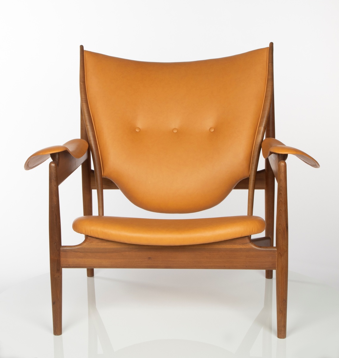 Stol, utført i brasiliansk valnøtt (imbuia). Åpen konstruksjon med fire runde ben, med størst tykkelse på midten, helt vertikalstilt. For- og bakben er forbundet med kraftig tverrligger som danner støtte for armlenene av buede stålplater. Mellom forbenene en bred sargsprosse som tiltar i høyde mot midtpartiet hvortil setets forkant er festet. Denne sprosse opptar i seg to kraftige, skråstilte og horisontale setestøtter fra bakbenene, og disse gir igjen feste for to spinkle, runde ryggstøtter som øverst møter bakbenene i en spiss vinkel, avsluttet med en liten knottforlengelse. Kraftige støttesprosser mellom bakbenene i rygghøyde samt kort tverrstøtte mot ryggplaten. Sete, rygg og armlener er fint og komfortabelt buet og trukket med lys oksehud. Stopning i sete og rygg. Både sete og armlener har få konsentrerte festepunkter til trekonstruksjonen og er skjult på undersiden. Dette gir sete og armlener en lett svevende virkning, som også understrekes av at setebredden er mindre enn trekonstruksjonens sitteåpning. Stolen har treets naturlige brune farge, med glattpusset overflate og avrundede kanter og hjørner.