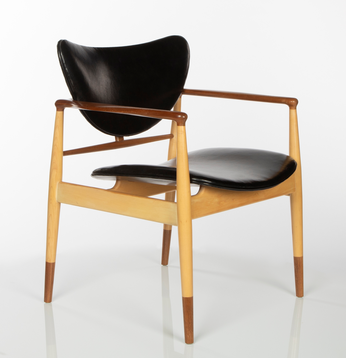 Stol av amerikaplatan (sycamore) og valnøtt. Åpen, lett konstruksjon. De fire runde ben er forbundet med lette sargstykker, samt to vertikale ryggspiler av forskjellig tykkelse og form. De helt horisontale, men fint avrundede armlenene danner bindeledd mellom for- og bakben. Treverket er vesentlig av lys amerikaplatan, med armlener, ryggsprosser og benenes "doppsko" i brun valnøtt. Stolen har stor sittebredde. Platene for rygg og sete er trukket med svart lær. Begge er lett buet med avrundede hjørner, ryggstykket har nærmest form som en liggende halvmåne. De er begge festet til trekonstruksjonen på få midtpunkter, hvilket gir den en svevende virkning; ryggstykket er tappet fast i ryggspilene, setet er festet på undersiden med fire jernbeslag og skruer til setets to underliggende sargstykker.