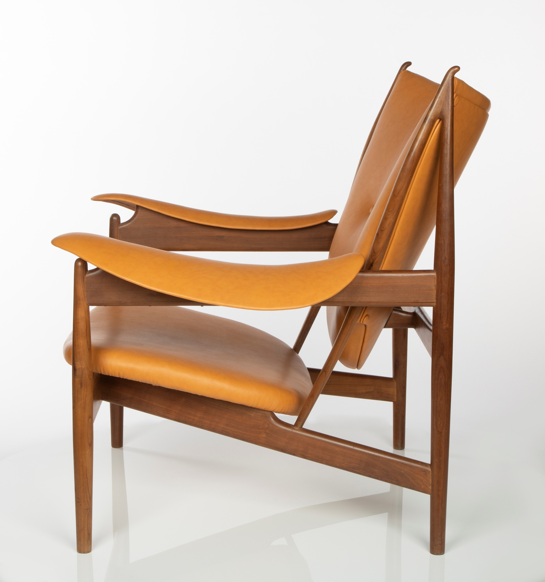 Stol, utført i brasiliansk valnøtt (imbuia). Åpen konstruksjon med fire runde ben, med størst tykkelse på midten, helt vertikalstilt. For- og bakben er forbundet med kraftig tverrligger som danner støtte for armlenene av buede stålplater. Mellom forbenene en bred sargsprosse som tiltar i høyde mot midtpartiet hvortil setets forkant er festet. Denne sprosse opptar i seg to kraftige, skråstilte og horisontale setestøtter fra bakbenene, og disse gir igjen feste for to spinkle, runde ryggstøtter som øverst møter bakbenene i en spiss vinkel, avsluttet med en liten knottforlengelse. Kraftige støttesprosser mellom bakbenene i rygghøyde samt kort tverrstøtte mot ryggplaten. Sete, rygg og armlener er fint og komfortabelt buet og trukket med lys oksehud. Stopning i sete og rygg. Både sete og armlener har få konsentrerte festepunkter til trekonstruksjonen og er skjult på undersiden. Dette gir sete og armlener en lett svevende virkning, som også understrekes av at setebredden er mindre enn trekonstruksjonens sitteåpning. Stolen har treets naturlige brune farge, med glattpusset overflate og avrundede kanter og hjørner.