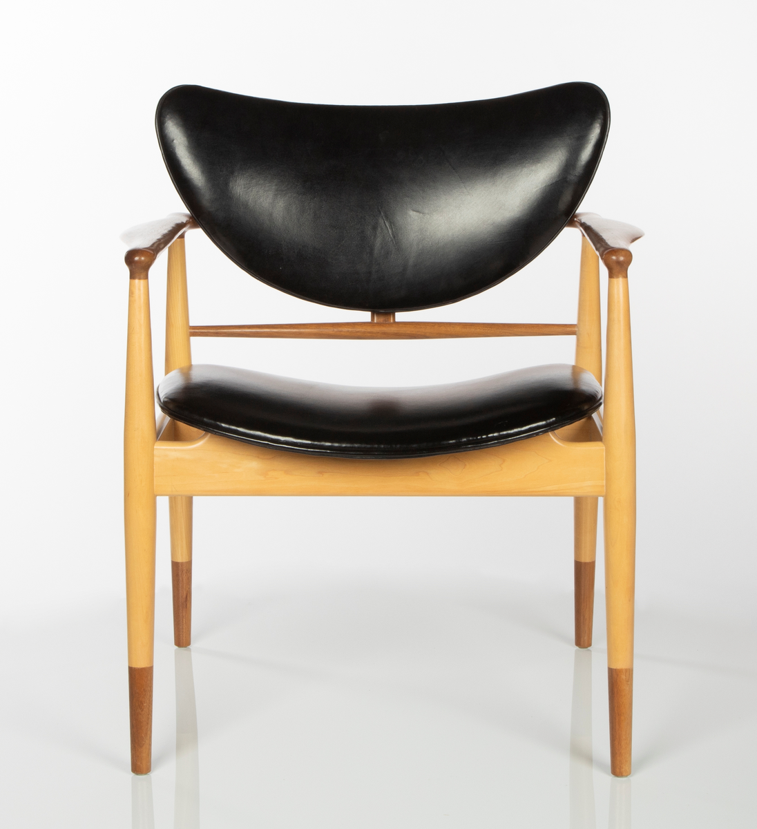 Stol av amerikaplatan (sycamore) og valnøtt. Åpen, lett konstruksjon. De fire runde ben er forbundet med lette sargstykker, samt to vertikale ryggspiler av forskjellig tykkelse og form. De helt horisontale, men fint avrundede armlenene danner bindeledd mellom for- og bakben. Treverket er vesentlig av lys amerikaplatan, med armlener, ryggsprosser og benenes "doppsko" i brun valnøtt. Stolen har stor sittebredde. Platene for rygg og sete er trukket med svart lær. Begge er lett buet med avrundede hjørner, ryggstykket har nærmest form som en liggende halvmåne. De er begge festet til trekonstruksjonen på få midtpunkter, hvilket gir den en svevende virkning; ryggstykket er tappet fast i ryggspilene, setet er festet på undersiden med fire jernbeslag og skruer til setets to underliggende sargstykker.