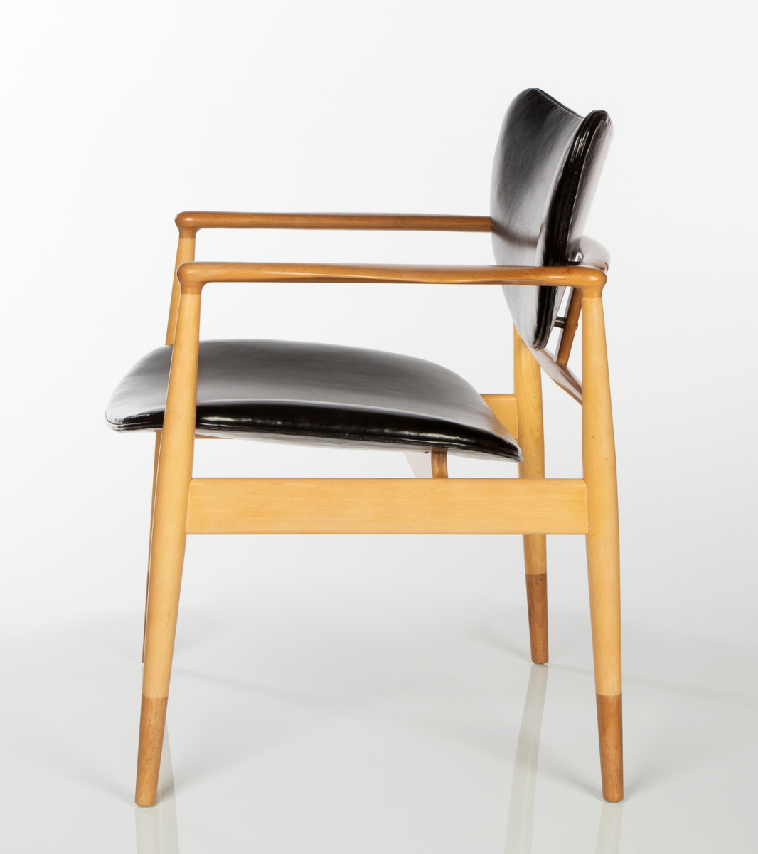 Stol av amerikaplatan (sycamore) og valnøtt. Åpen, lett konstruksjon. De fire runde ben er forbundet med lette sargstykker, samt to vertikale ryggspiler av forskjellig tykkelse og form. De helt horisontale, men fint avrundede armlenene danner bindeledd mellom for- og bakben. Treverket er vesentlig av lys amerikaplatan, med armlener, ryggsprosser og benenes "doppsko" i brun valnøtt. Stolen har stor sittebredde. Platene for rygg og sete er trukket med svart lær. Begge er lett buet med avrundede hjørner, ryggstykket har nærmest form som en liggende halvmåne. De er begge festet til trekonstruksjonen på få midtpunkter, hvilket gir den en svevende virkning; ryggstykket er tappet fast i ryggspilene, setet er festet på undersiden med fire jernbeslag og skruer til setets to underliggende sargstykker.