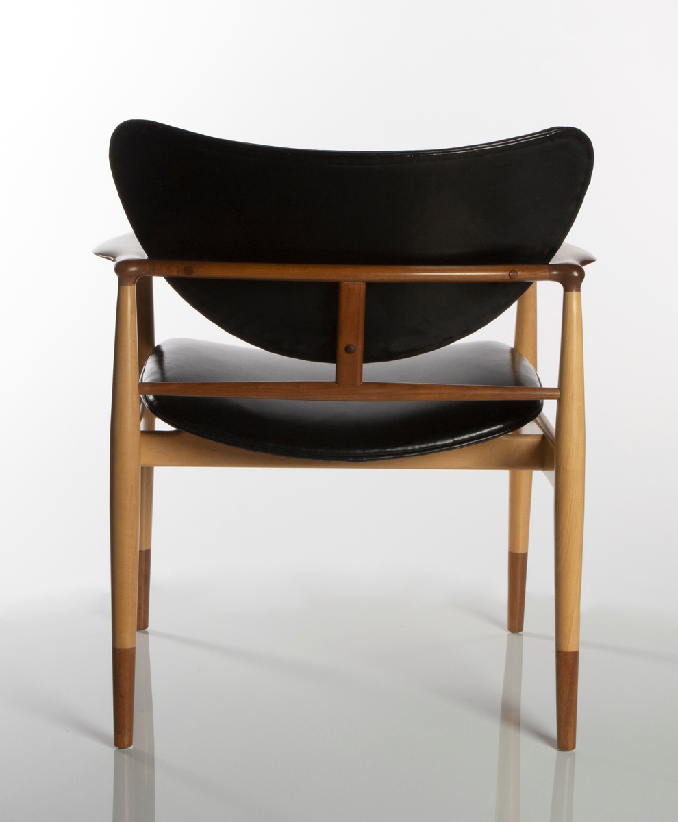 Stol av amerikaplatan (sycamore) og valnøtt. Åpen, lett konstruksjon. De fire runde ben er forbundet med lette sargstykker, samt to vertikale ryggspiler av forskjellig tykkelse og form. De helt horisontale, men fint avrundede armlenene danner bindeledd mellom for- og bakben. Treverket er vesentlig av lys amerikaplatan, med armlener, ryggsprosser og benenes "doppsko" i brun valnøtt. Stolen har stor sittebredde. Platene for rygg og sete er trukket med svart lær. Begge er lett buet med avrundede hjørner, ryggstykket har nærmest form som en liggende halvmåne. De er begge festet til trekonstruksjonen på få midtpunkter, hvilket gir den en svevende virkning; ryggstykket er tappet fast i ryggspilene, setet er festet på undersiden med fire jernbeslag og skruer til setets to underliggende sargstykker.