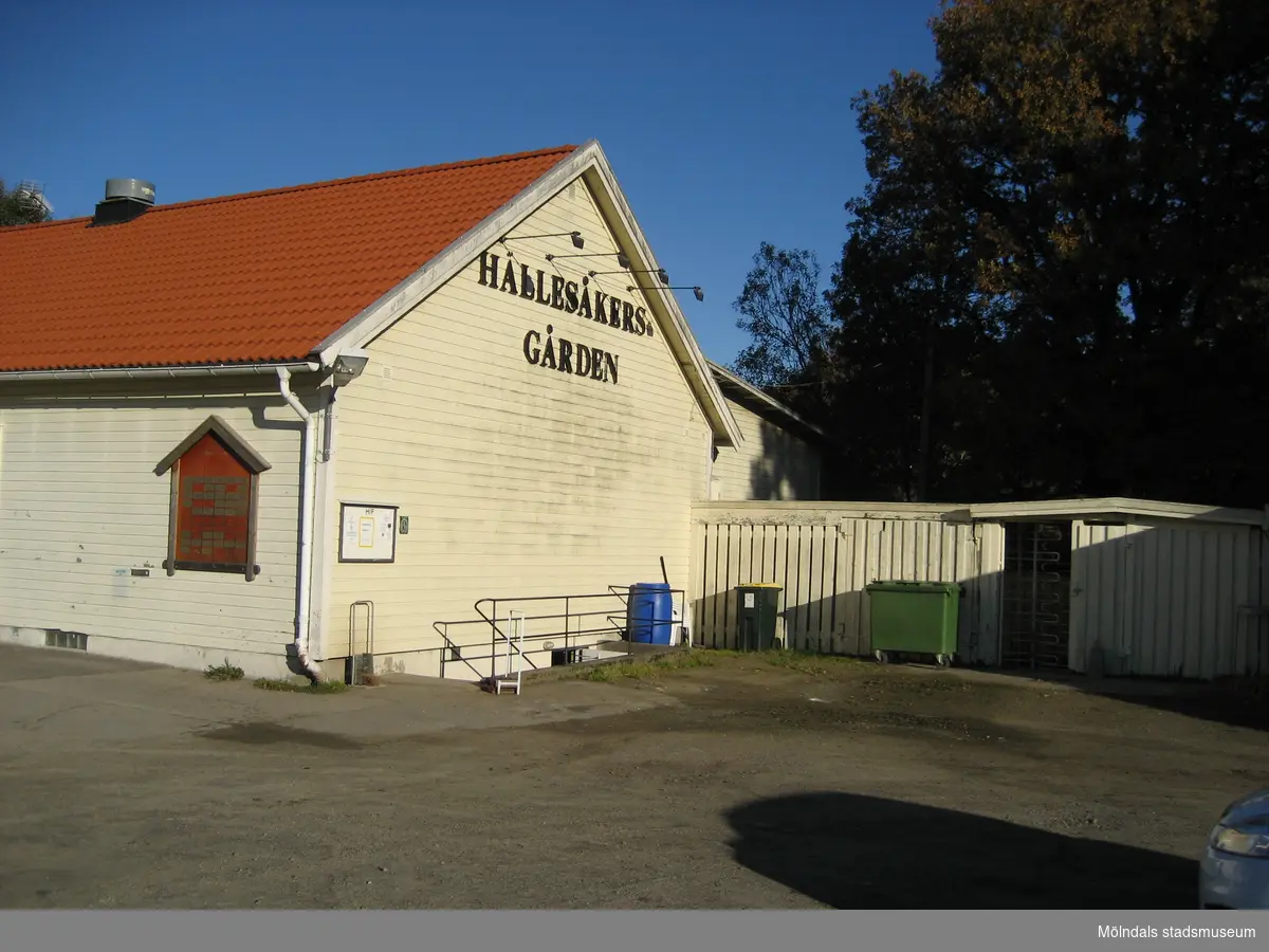 Hörnet av den ljusgula Hällesåkersgården år 2010. På gavelns övre del står textat med versaler HÄLLESÅKERSGÅRDEN. Till höger ses ett staket med en rotationsgrind.
Relaterade motiv: 2024_1119 - 1137.