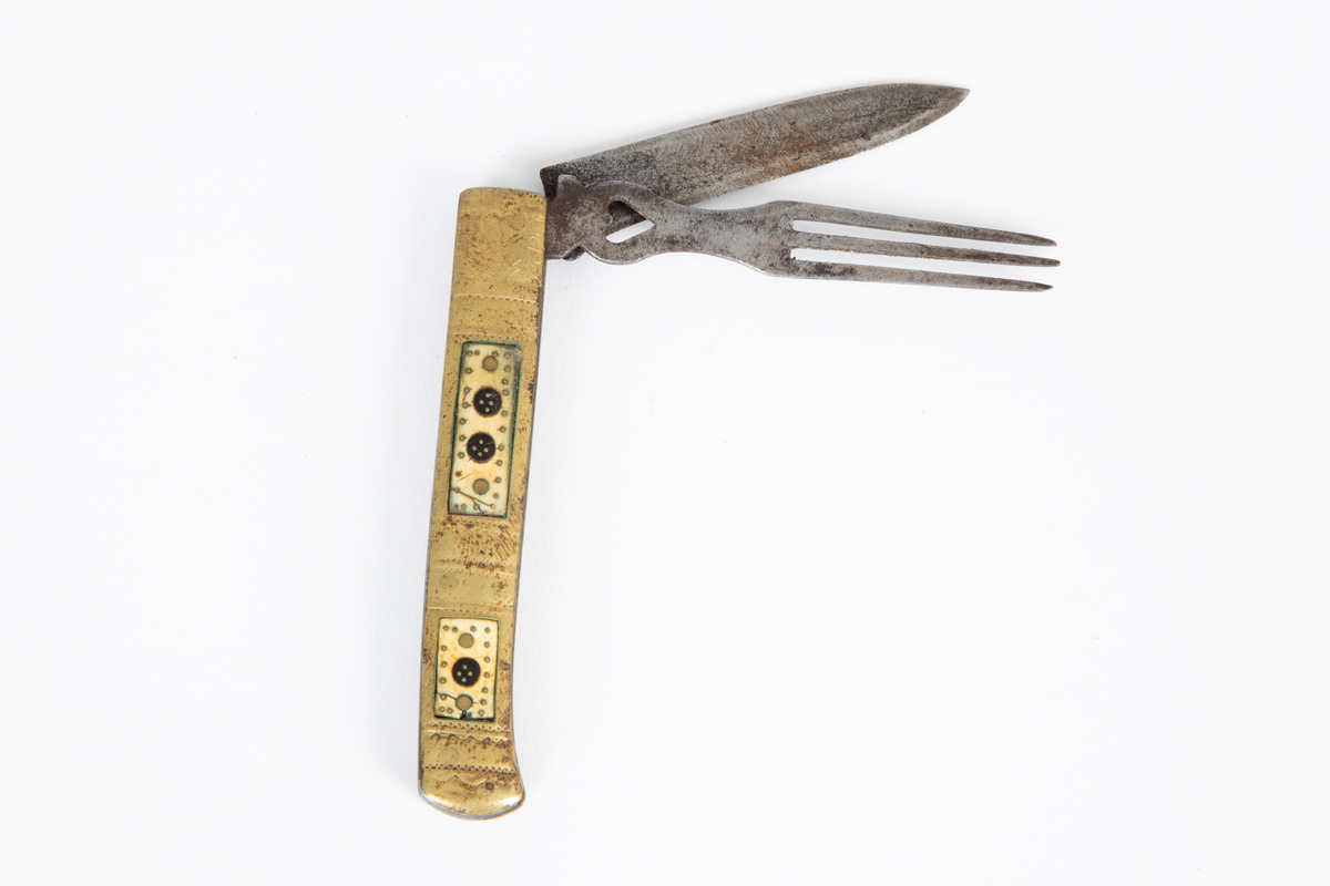 Foldekniv med kniv og gaffel. Kniven er spiss og har nærmest lansettform. Gaffelen rett og flat med 3 tenner og gjennombrutt hjerteform nær roten. Skaftet består av to sammenføyde messingplater som på hver side har innlagt rektangulære felt av horn igjen innlagt med messing. Siselert dekor på messingskaftet med buer og prikker.