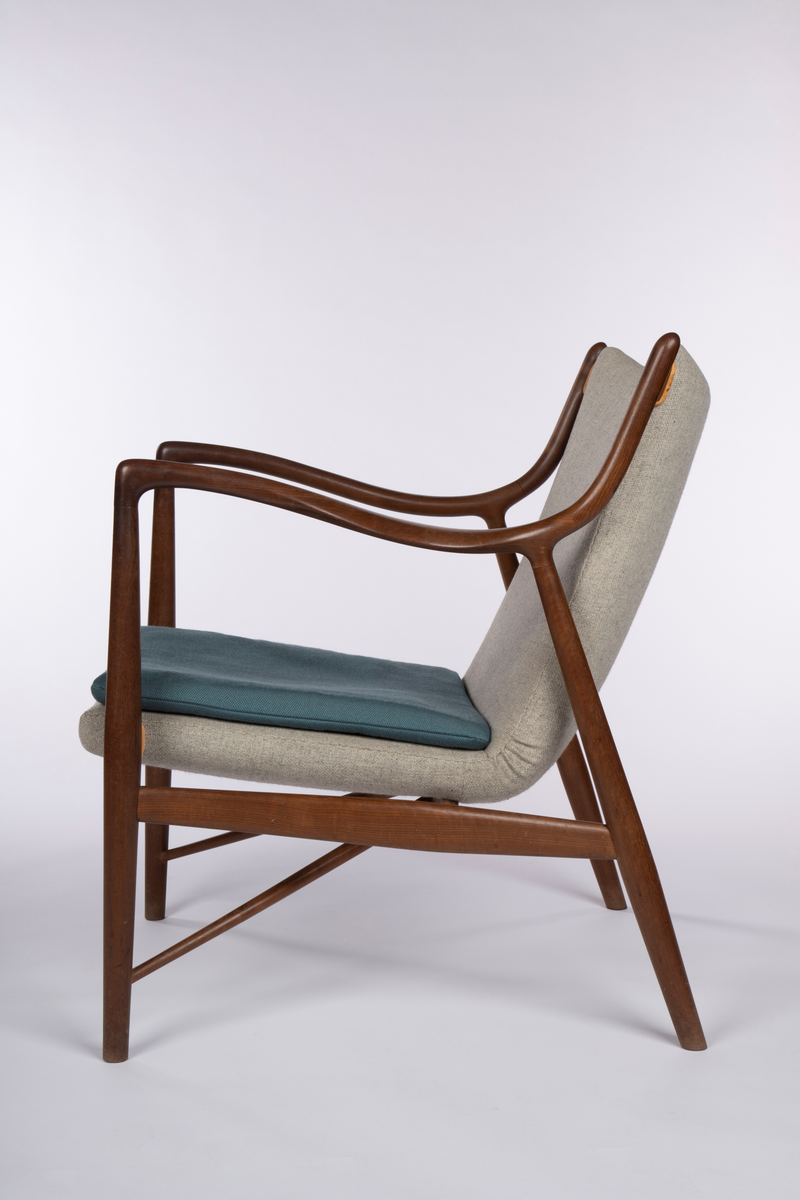 Stol i åpen, lett konstruksjon med vertikalstilte forben, og sterkt skråstilte bakben. Mykt svungne armlener festet med jevn overgang til for- og bakben, og som herfra er svunget opp som akterstaver. Disse er forbundet med et ryggbrett som er skjult av stopningen. Overgangene på sidene er kantet med lyst lær. Mellom de to sidesargene, som også fungerer som sidesprosser, et midtstykke som støtte for setet. Dreiede sprosser løpter fra nederst på forbenene på skrå opp til midtstykket. Mellom forbenene er forsargen skjult av stopningen og kantet med lyst lær på hver side. Sammenhengende sete- og ryggstopning, trukket med grått ullstoff med løs pute i blågrønt ullstoff.