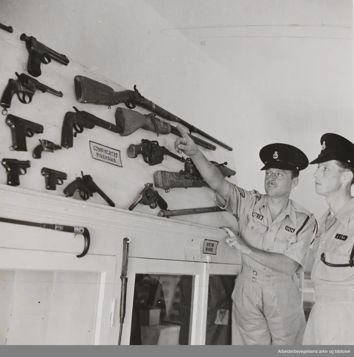 Palestina 1947. Bildetekst Arbeiderbladet: "Politiet i Palestina har etterhvert fått en anseelig samling konfiskerete våpen. En sersjant viser noen våpentyper til en ny mann i politistyrken. "
