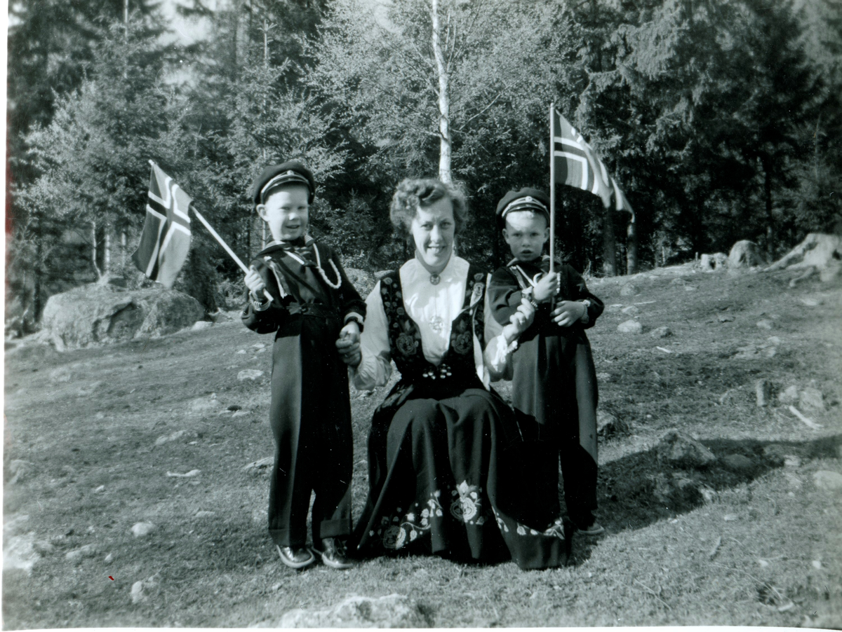 Portrett av dame med bunad og 2 gutter med flagg.