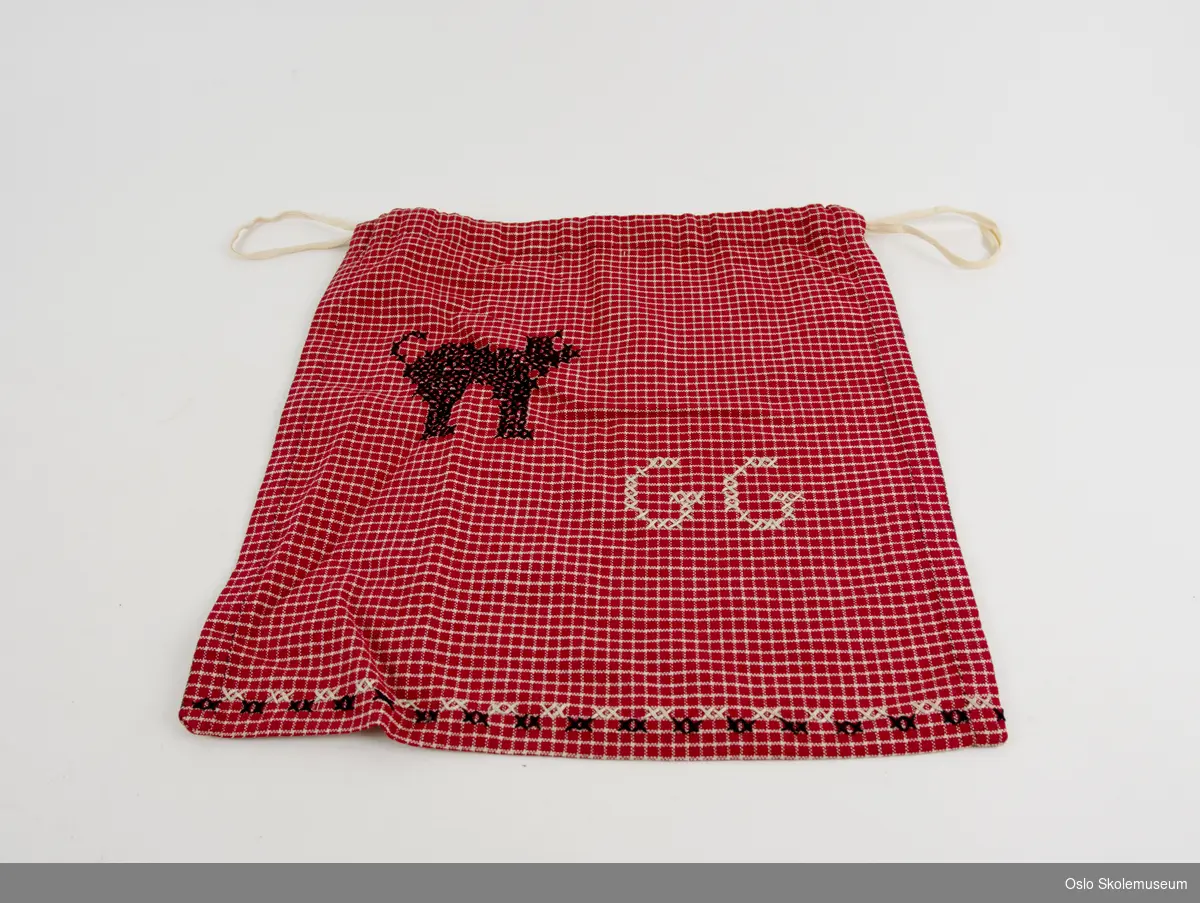 Håndarbeidspose i hvit- og rødrutete tekstil. Nederst på psen er det brodert en bord med svart og hvit tråd. På posen er det brodert en svart katt samt bokstavene "GG" med hvit tråd. Posen kan snurpes sammen.