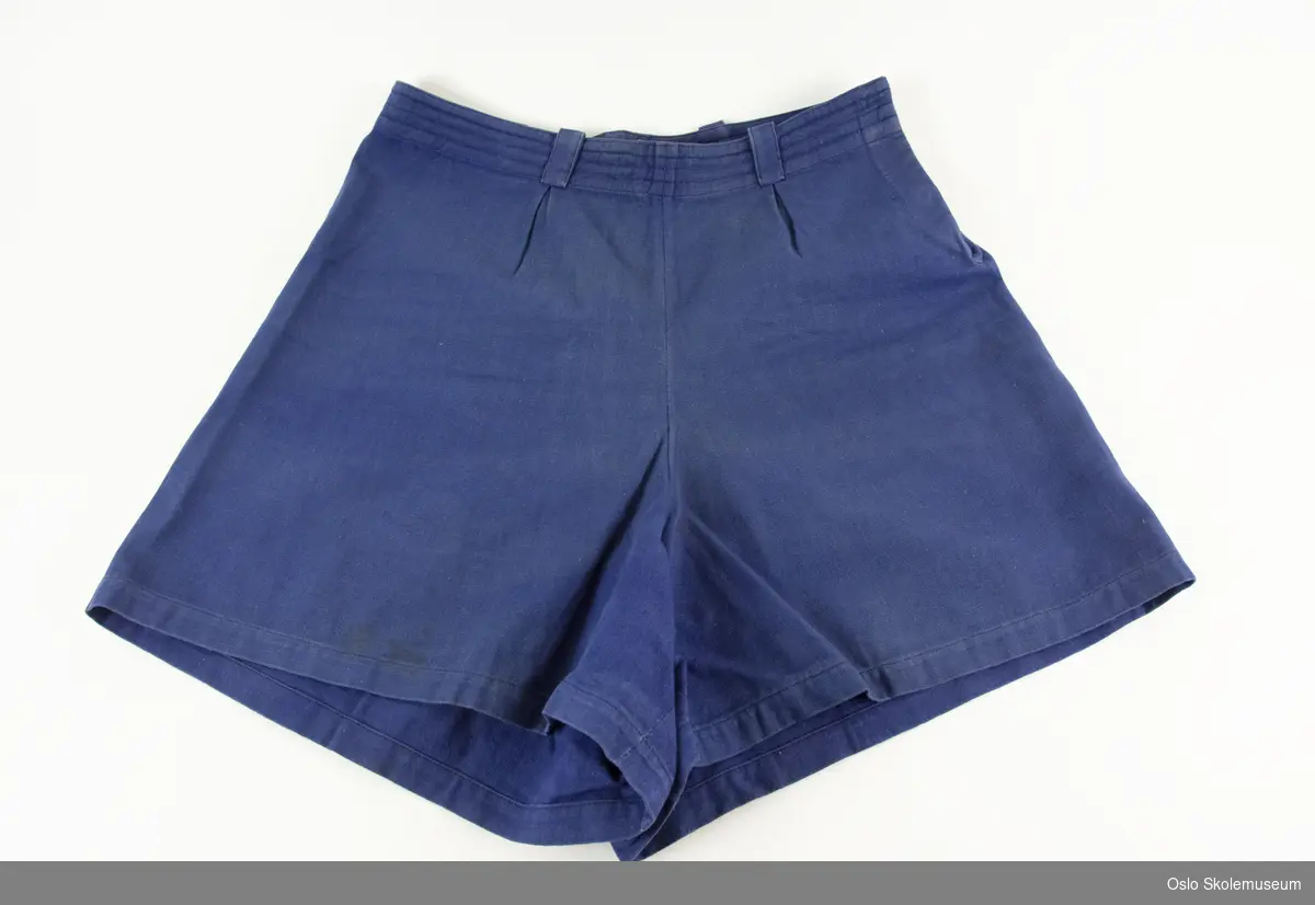 Shorts i blått tekstil. Shortsen har lukking (knapp og hemper) i den ene siden.