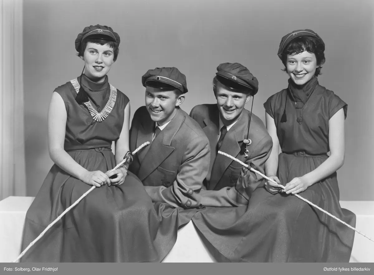Gruppeportrett av russ 1955, personene er ukjente. Antakelig gymnasiaster fra Sarpsborg. Med russelue og russeknute og russestokk av bambus. Atelierfoto.