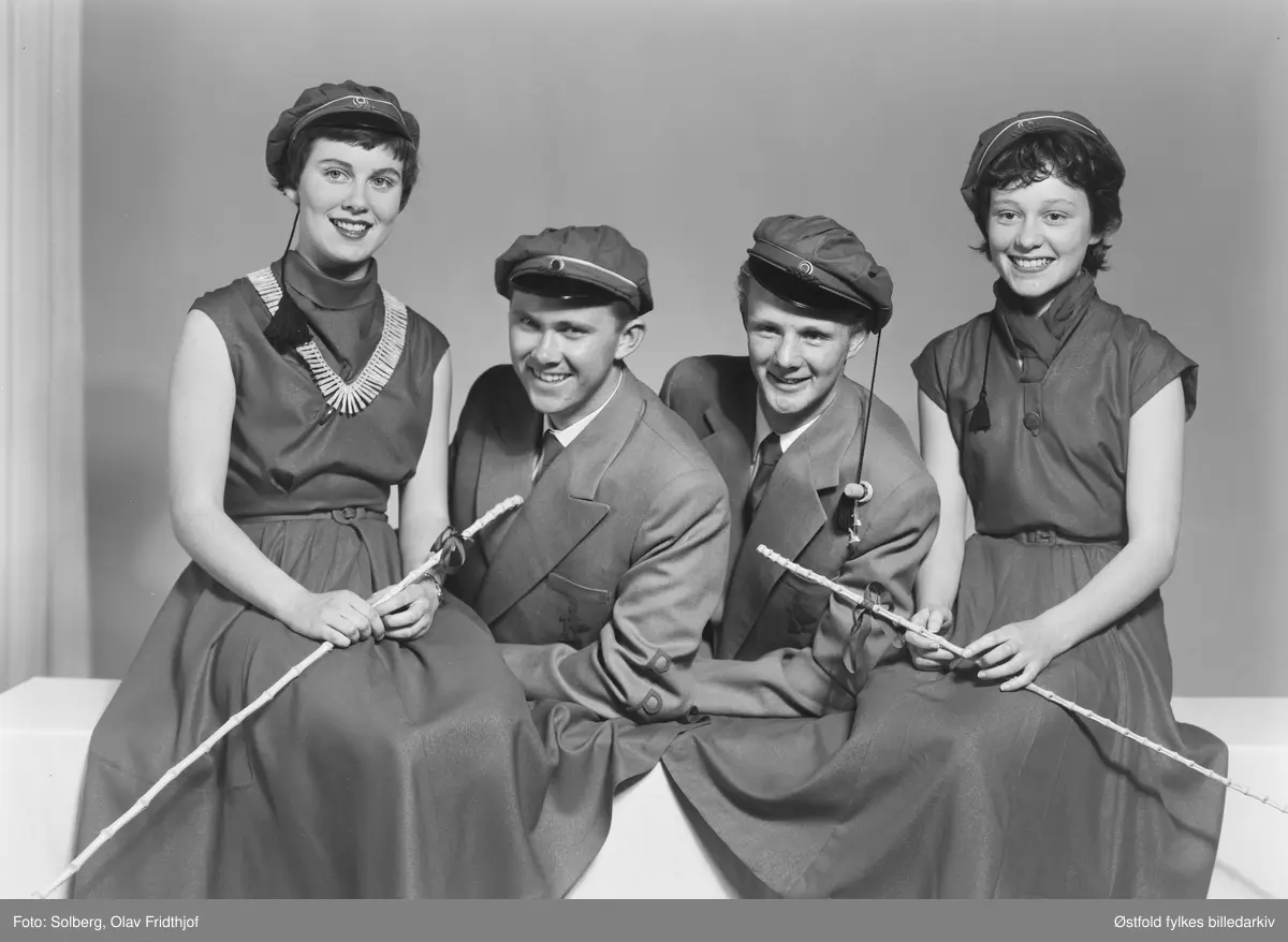 Gruppeportrett av russ 1955, personene er ukjente. Antakelig gymnasiaster fra Sarpsborg. Med russelue og russeknute og russestokk av bambus. Atelierfoto.