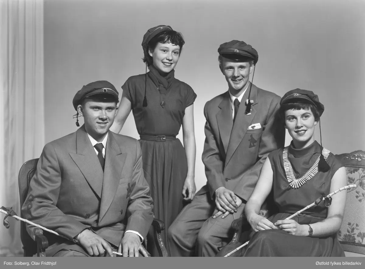 Gruppeportrett av russ 1955, personene er ukjente. Antakelig gymnasiaster fra Sarpsborg. Med russelue og russeknute og russestokk av bambus. Atelierfoto.