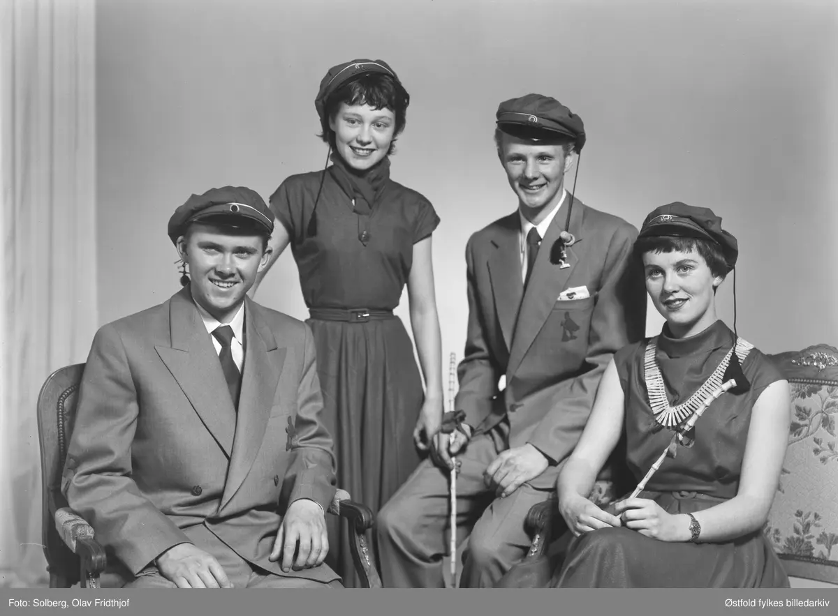Gruppeportrett av russ 1955, personene er ukjente. Antakelig gymnasiaster fra Sarpsborg. Med russelue og russeknute og russestokk av bambus. Atelierfoto.