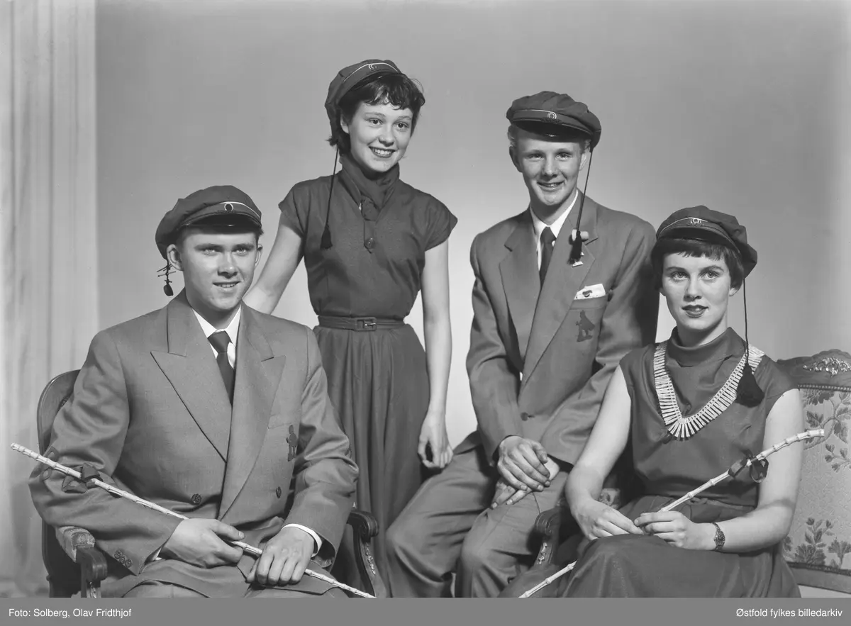 Gruppeportrett av russ 1955, personene er ukjente. Antakelig gymnasiaster fra Sarpsborg. Med russelue og russeknute og russestokk av bambus. Atelierfoto.