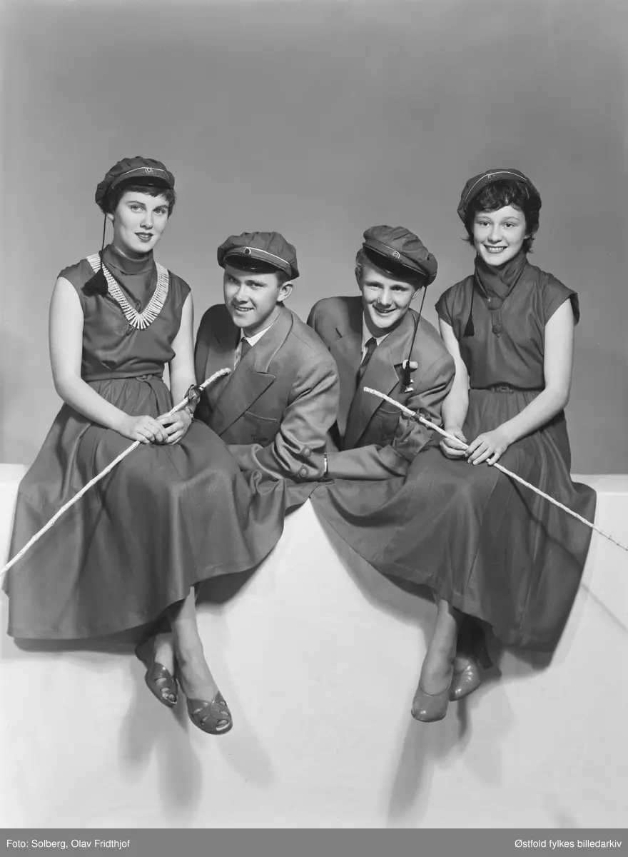 Gruppeportrett av russ 1955, personene er ukjente. Antakelig gymnasiaster fra Sarpsborg. Med russelue og russeknute og russestokk av bambus. Atelierfoto.