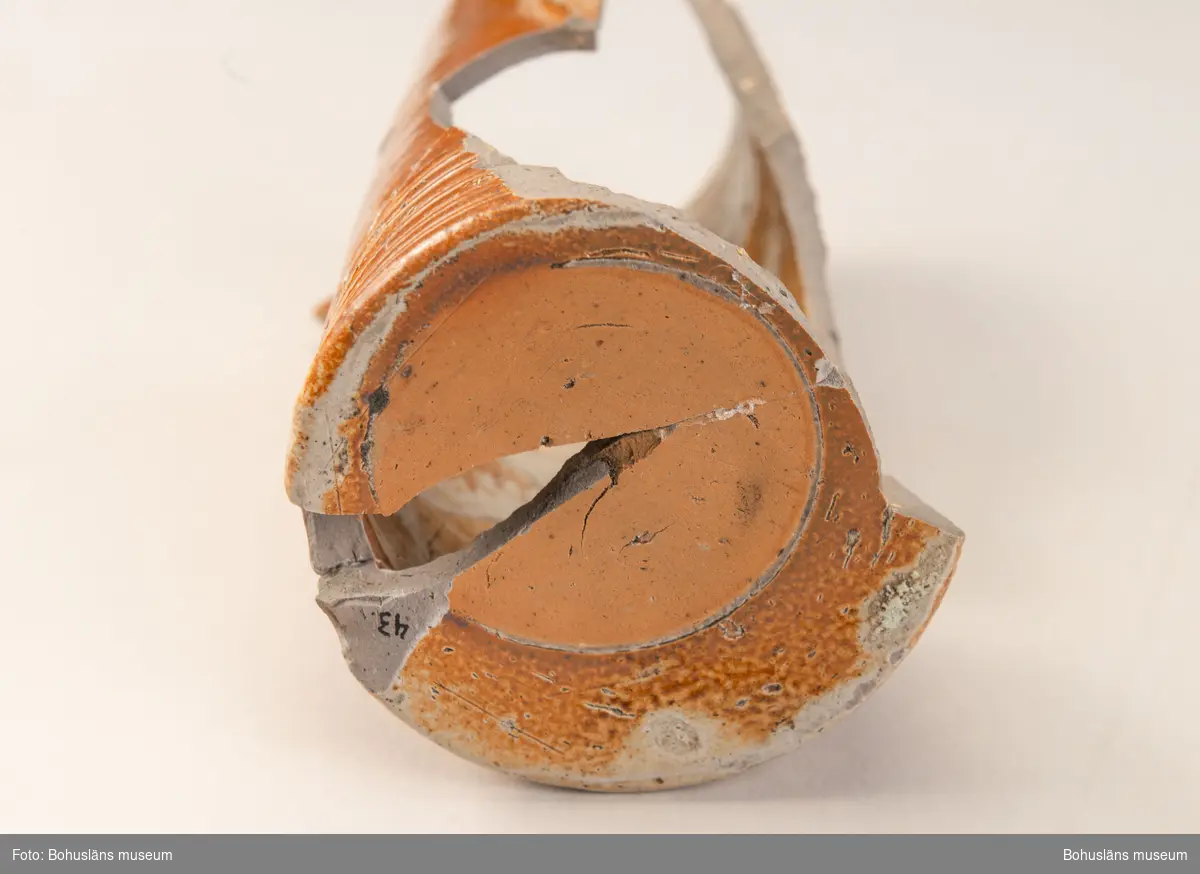 Krus/Kanna. Stort brunglaserat stengodskärl med dekor i form av delvis bevarad textmedaljong på framsida kanna. Tysk text. 

Landskap: Bohuslän