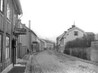 Parti av Skönbergsgatan i Söderköping 1918. Vy från mötet av den senare utlagda Barnhemsgatan med blicken vänd österut. Närmast till vänster skomakare Carl Johan Hammarlunds verkstad med affär.