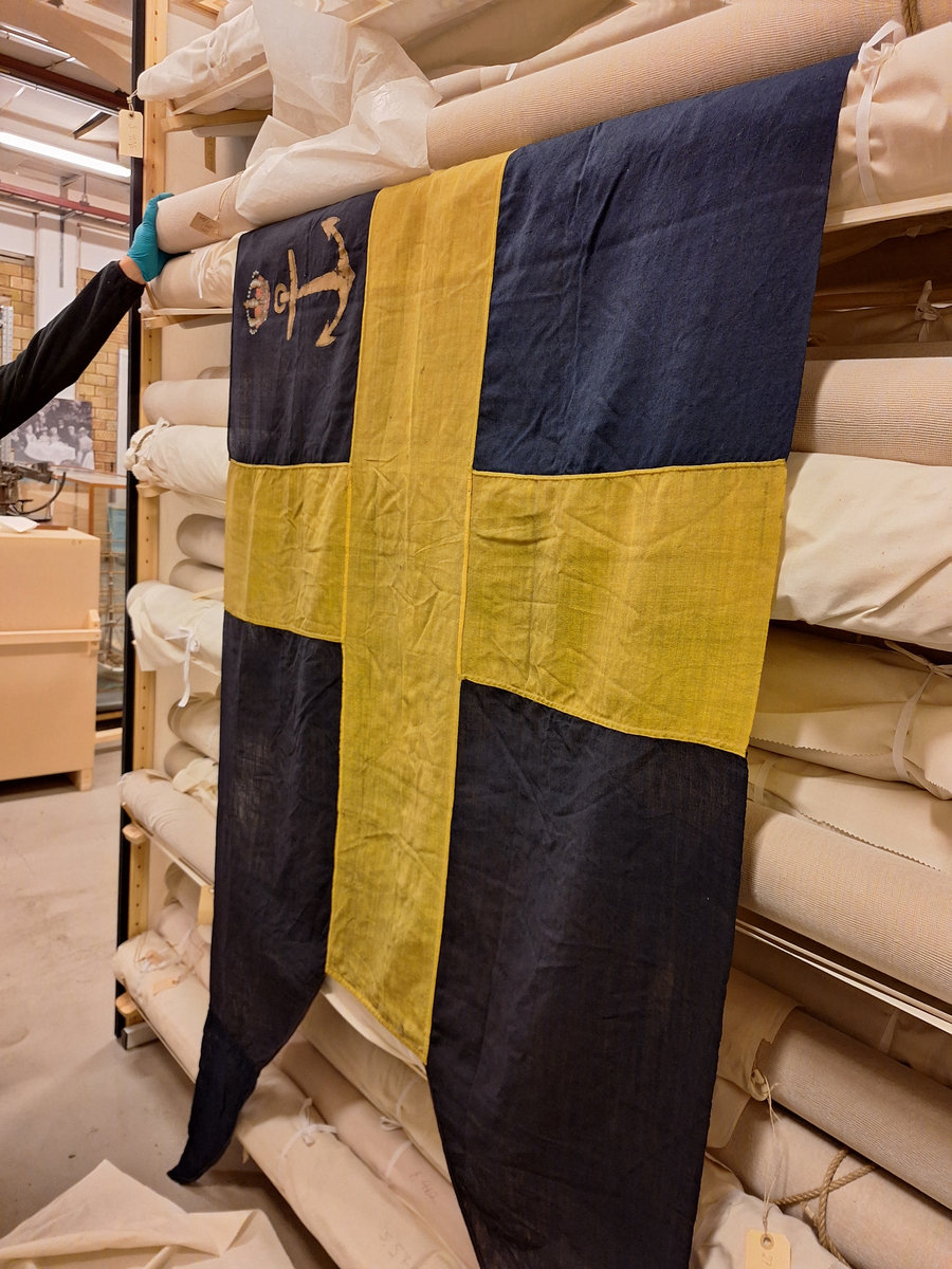 Lotsflagga av bomull. Svensk tvåtungad flagga med Kgl. Lotsverkets emblem med krona över i övre inre fältet. Tamp med lekare.