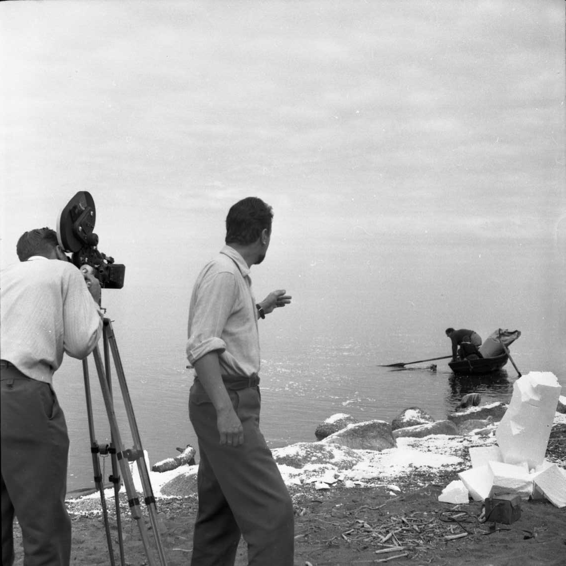 Ett filmteam vid Vätterstranden, norr om hamne i Gränna, lite publik i bakgrunden. Konstgjord snö på stranden. En roddbåt är på väg mot stranden.